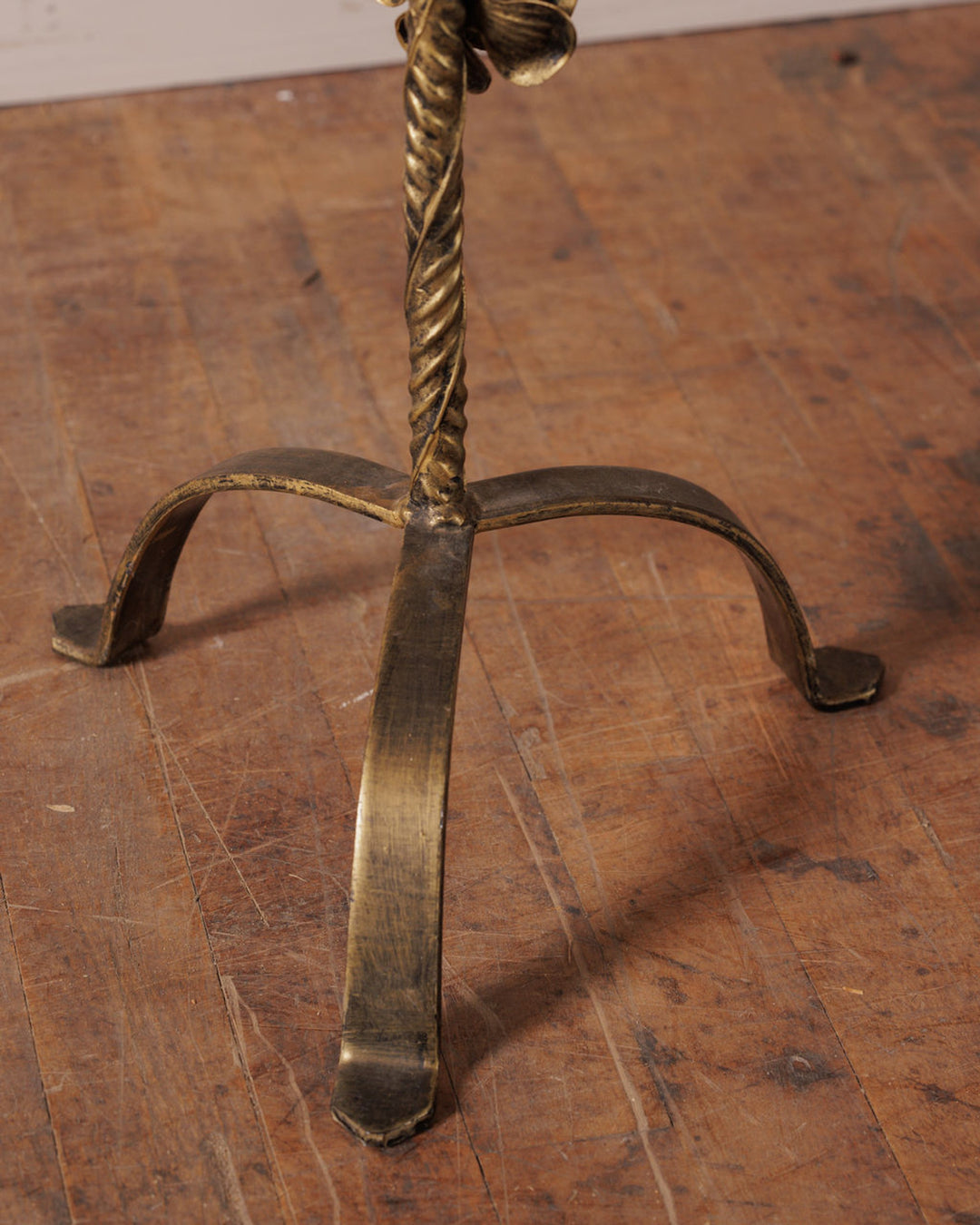 Antique brass tripod stand with a twisted stem on a wooden floor.