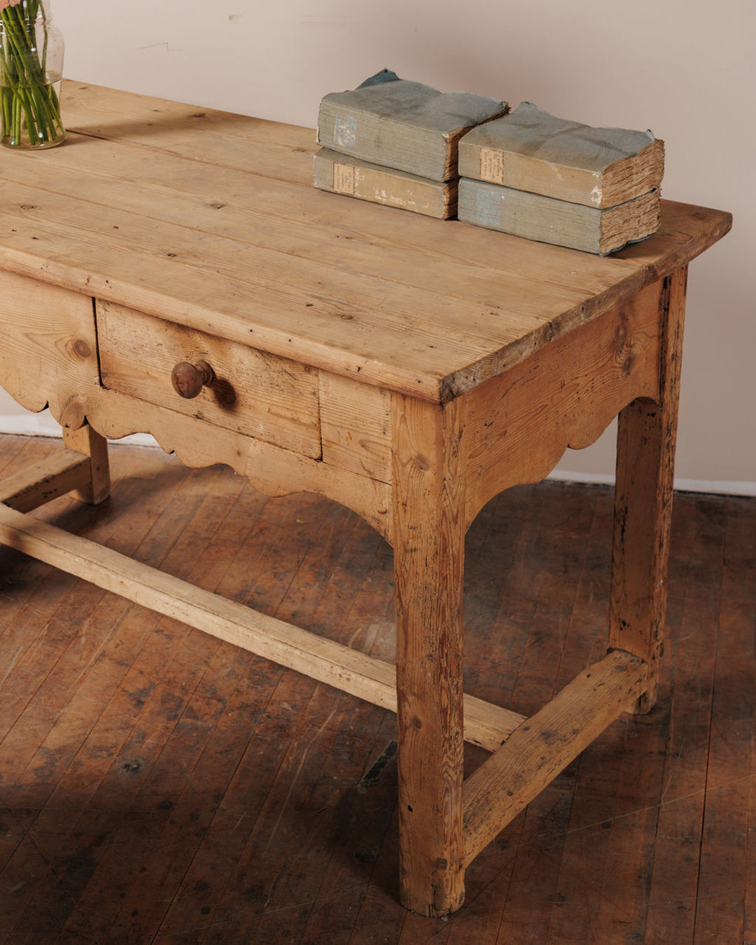 Rustic wooden table with a drawer, scalloped apron, and two stacks of old blue books.