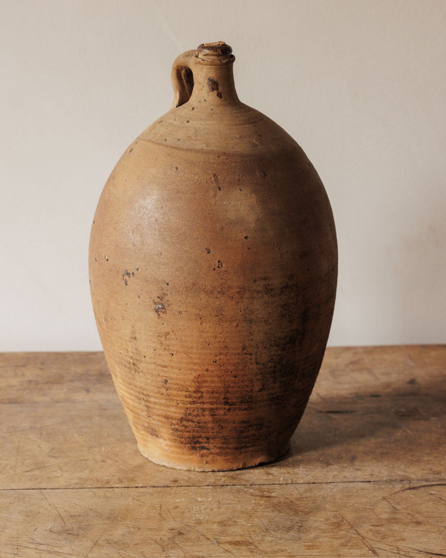 Rustic brown pottery jug with a handle on a wooden table.