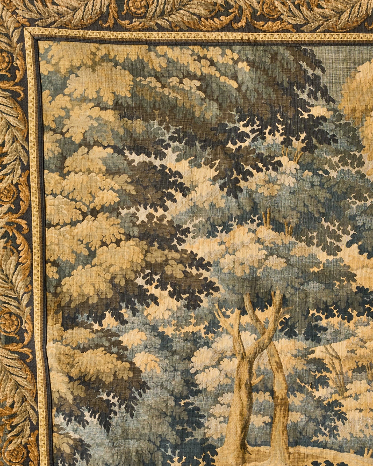 Woven tapestry depicting a dense forest in muted blues, greens, and golds, with an ornate, leaf-patterned border.