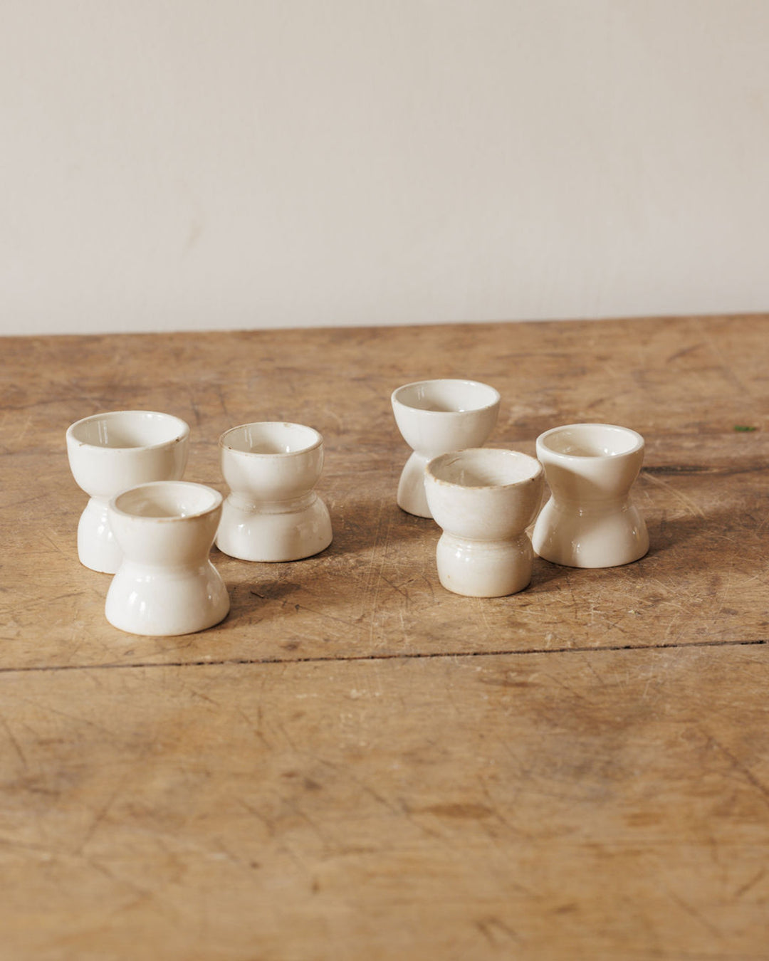 Six white ceramic egg cups on a wooden table.