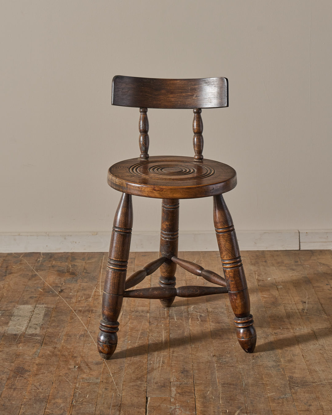 Dark wooden stool with a backrest and a carved round seat.