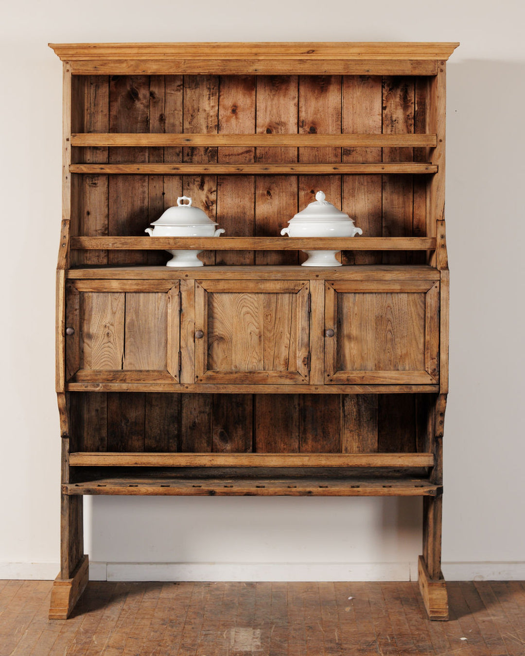 Rustic wooden hutch with open shelves, cabinets, and two white tureens.