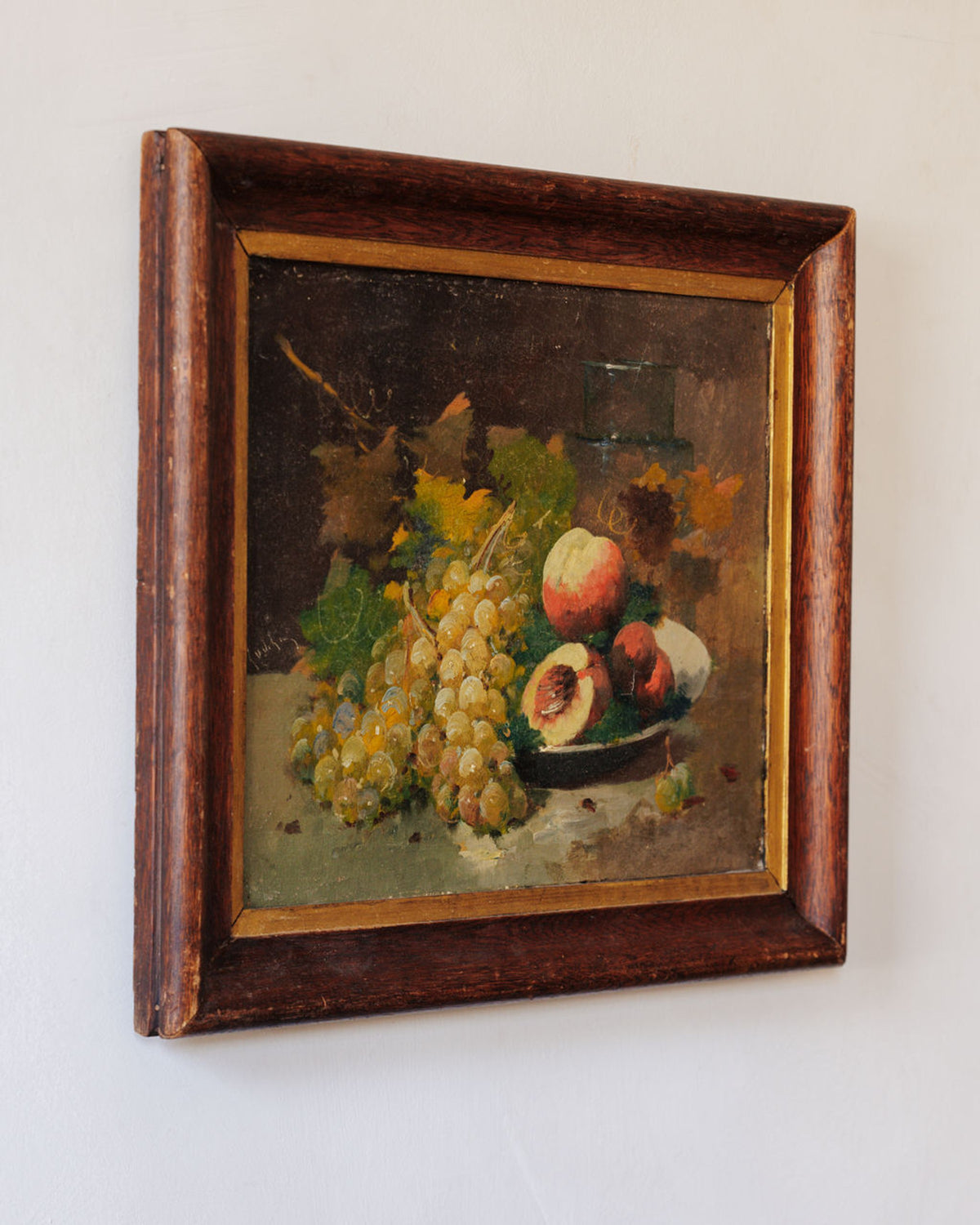 Still life painting of grapes and peaches in a dark wooden frame.