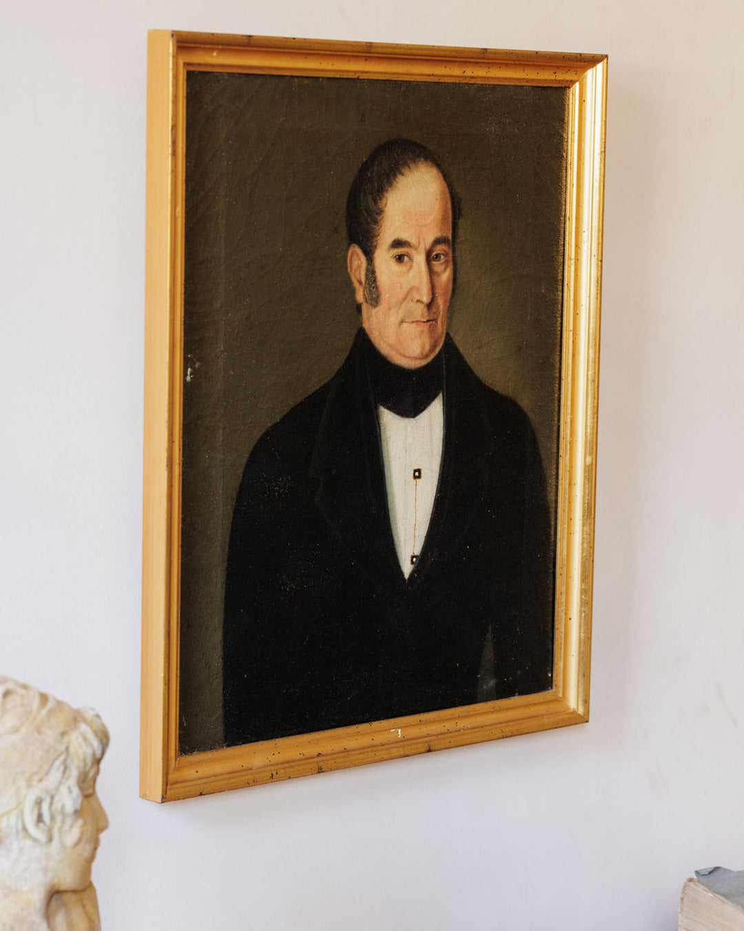An antique portrait painting of a man in a dark suit and white shirt, in a gold frame.