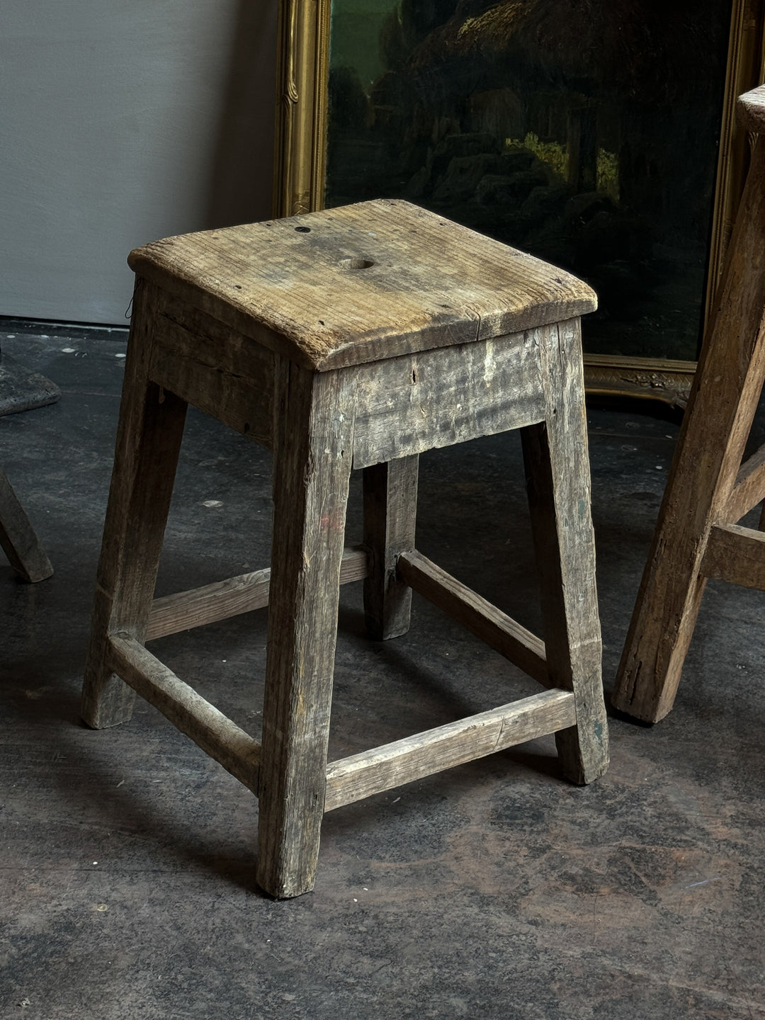 a wooden stool is sitting on a concrete floor next to a painting .