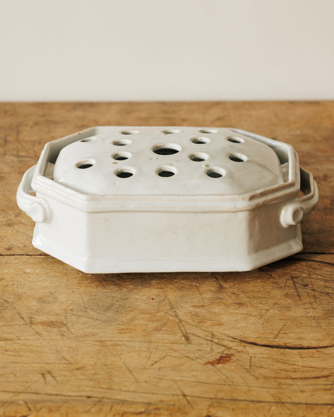 White octagonal ceramic flower brick with holes on its lid, on a wooden surface.