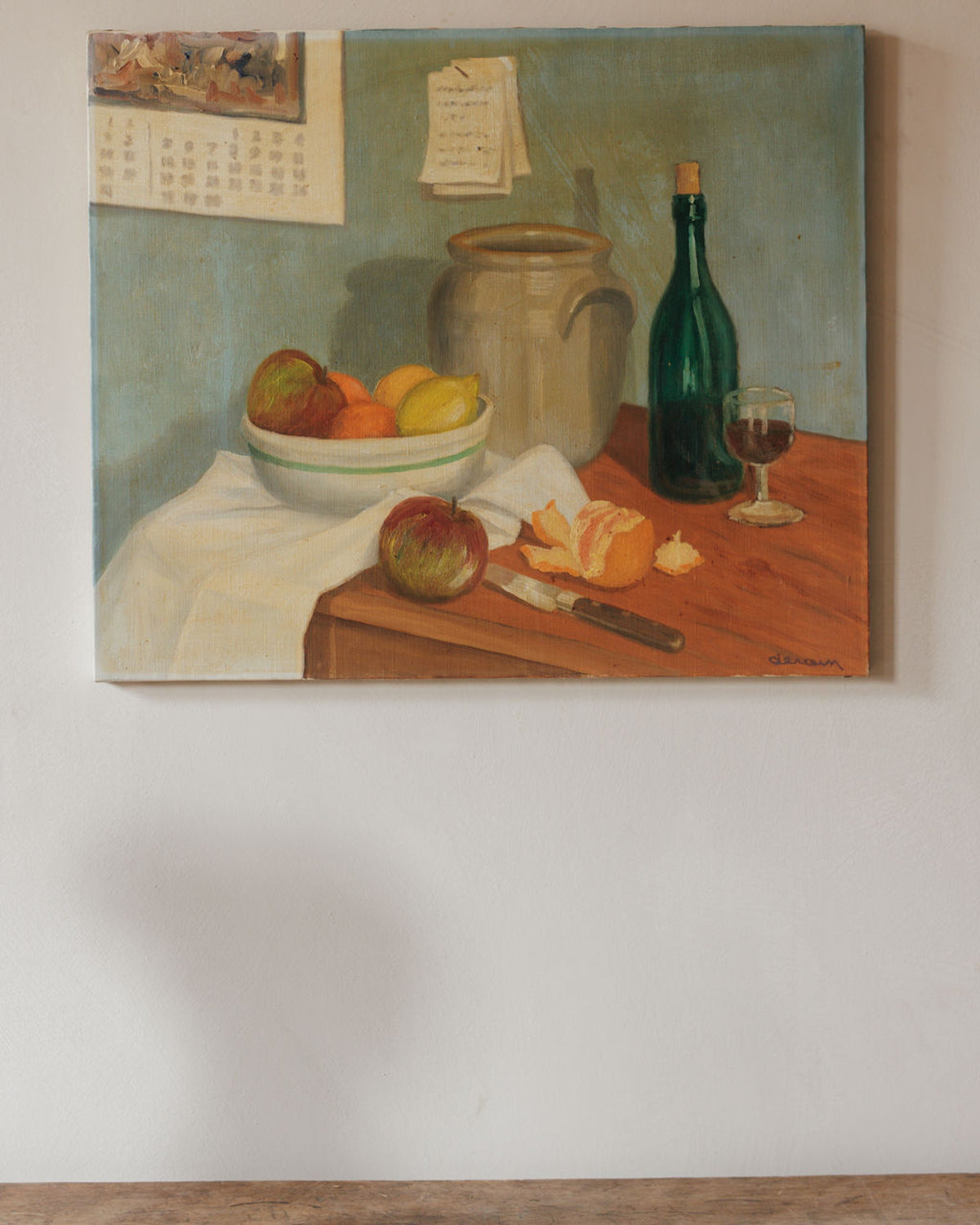 Still life painting featuring a bowl of fruit, a wine bottle, a glass of wine, and a peeled orange on a wooden table, with a calendar on the wall above.