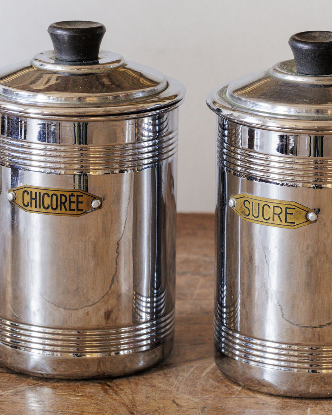 Two vintage silver canisters, labeled "CHICORÉE" and "SUCRE", on a wooden surface.