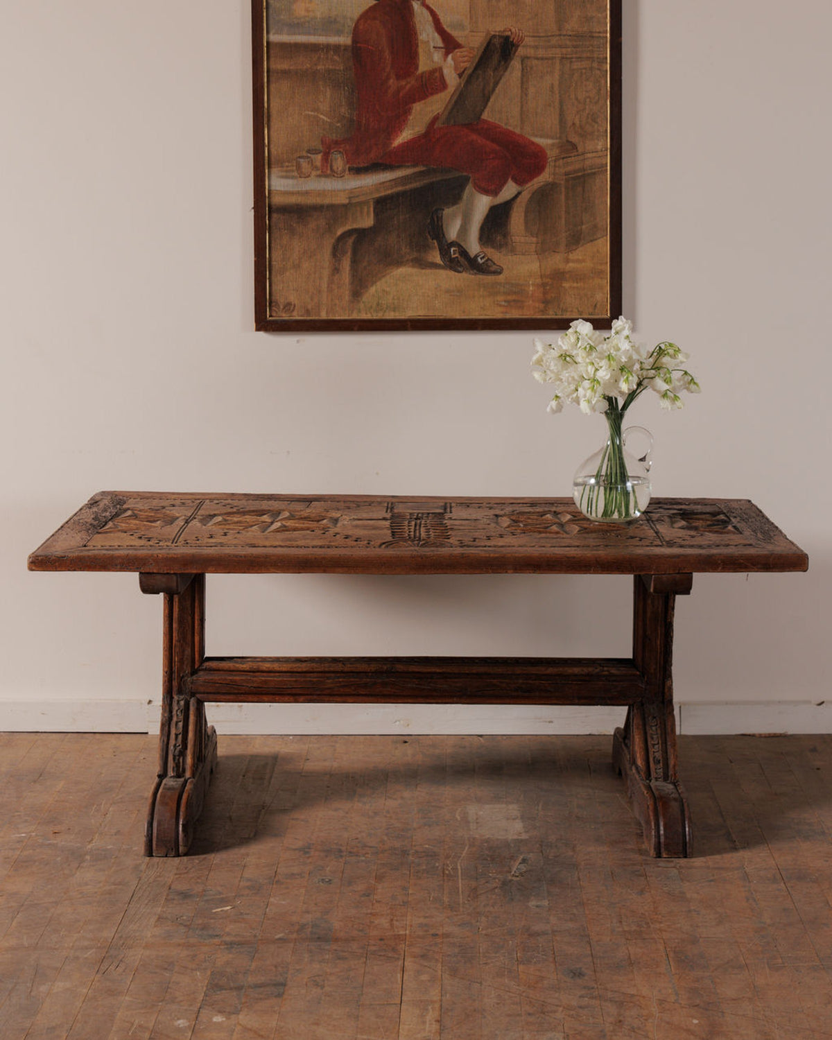 A carved wooden table with a vase of white flowers sits under a painting of a man in red.