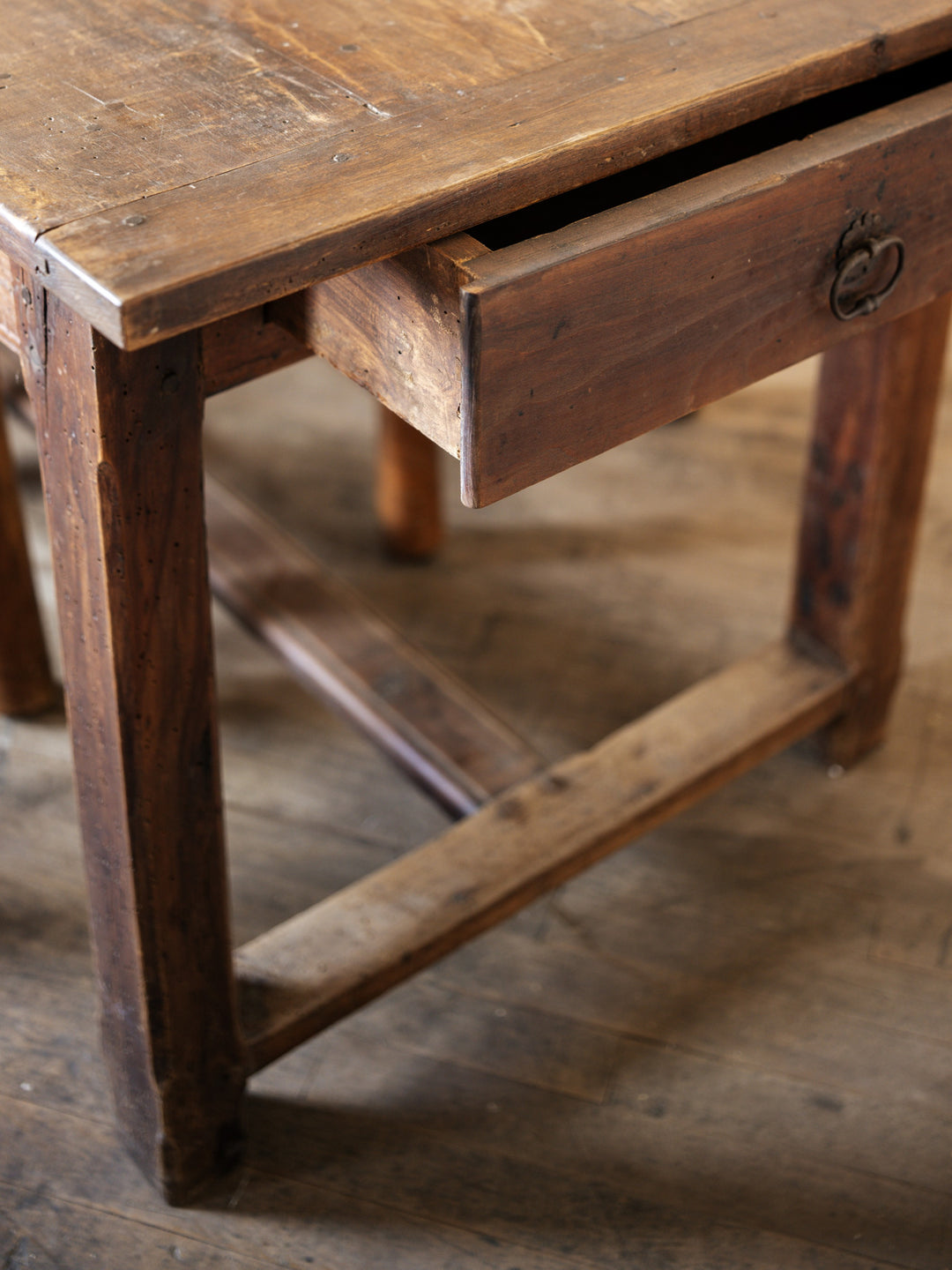 a walnut french farm table with a drawer open on a wooden floor