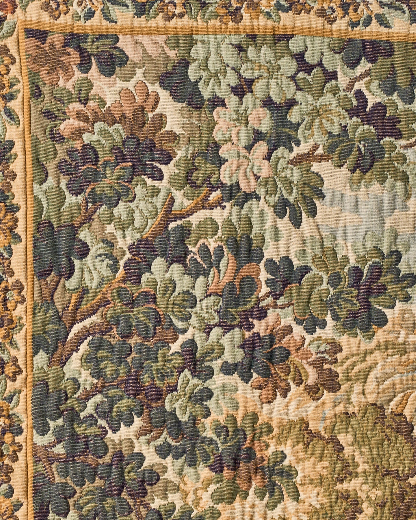 Close-up of a woven tapestry showing trees and leaves in muted greens and browns, with a patterned border.
