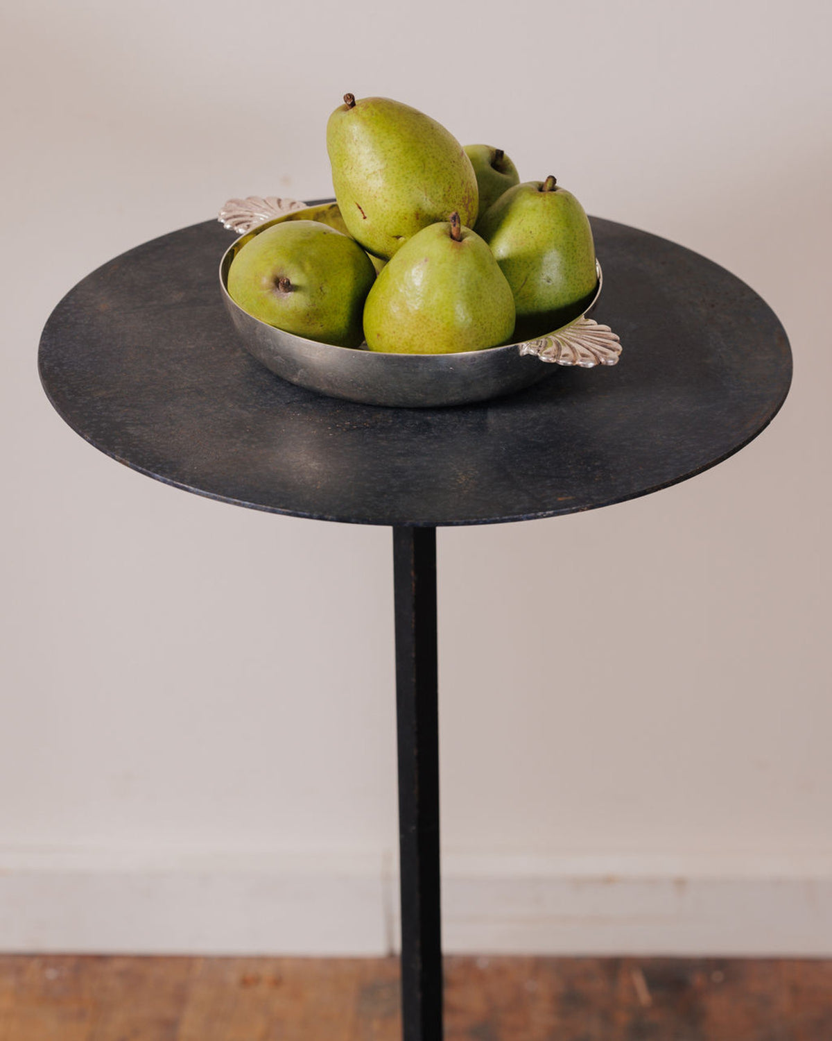Green pears in a silver bowl on a dark metal table.