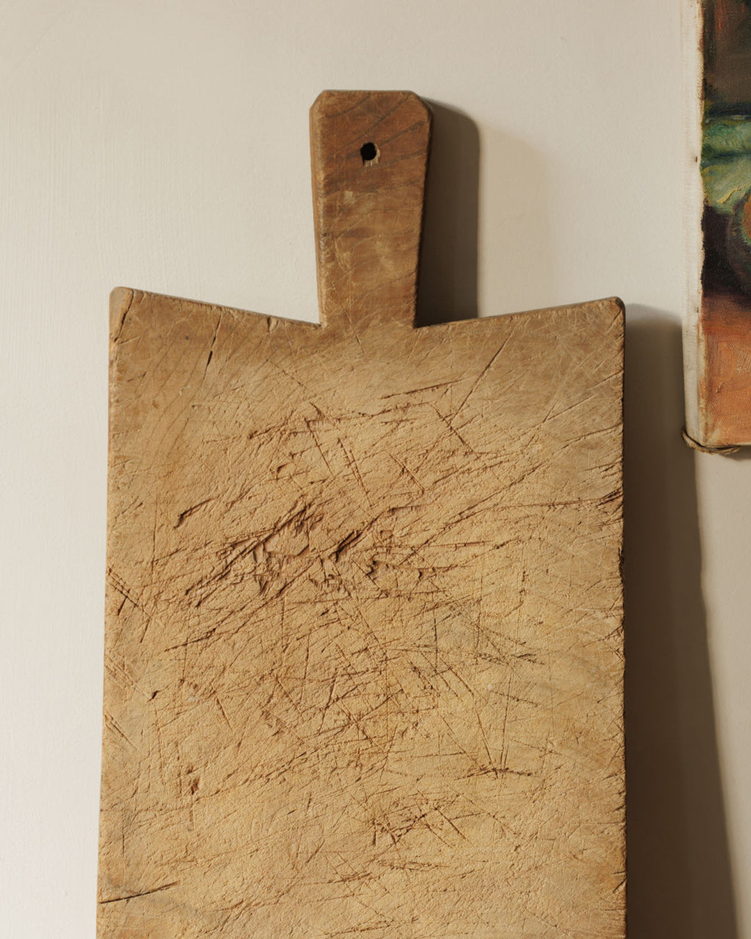 A well-worn wooden cutting board with a handle and numerous knife marks.