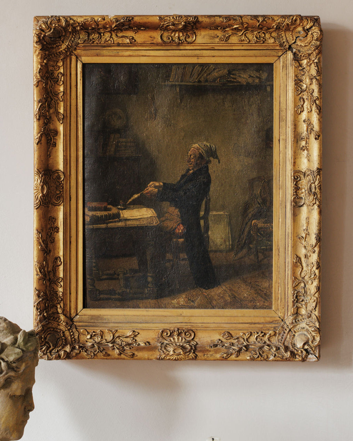 Painting of an old man writing at a desk in an ornate gold frame, with a partial bust in the foreground.