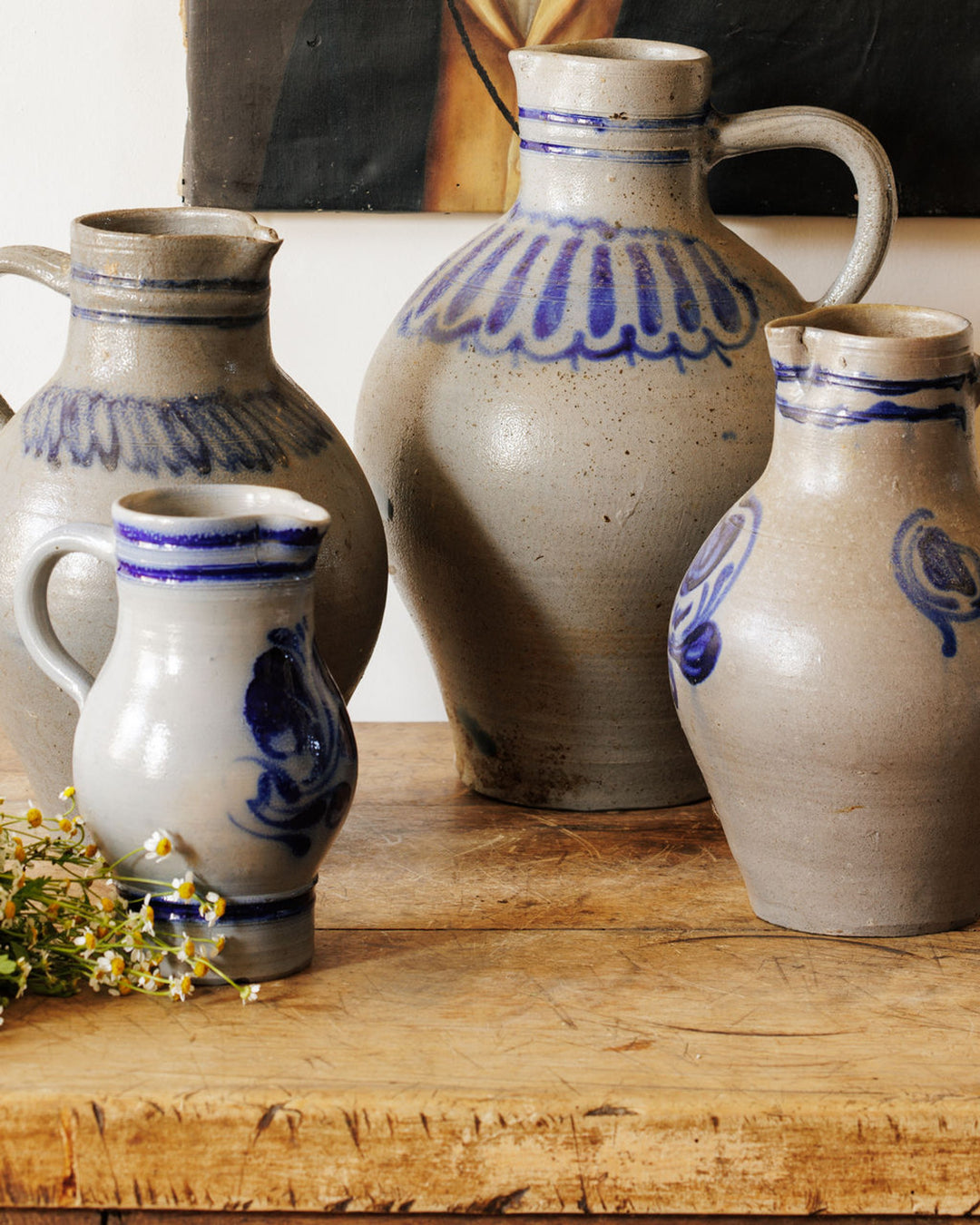 Four grey pottery jugs with blue patterns on a wooden table, next to chamomile flowers.