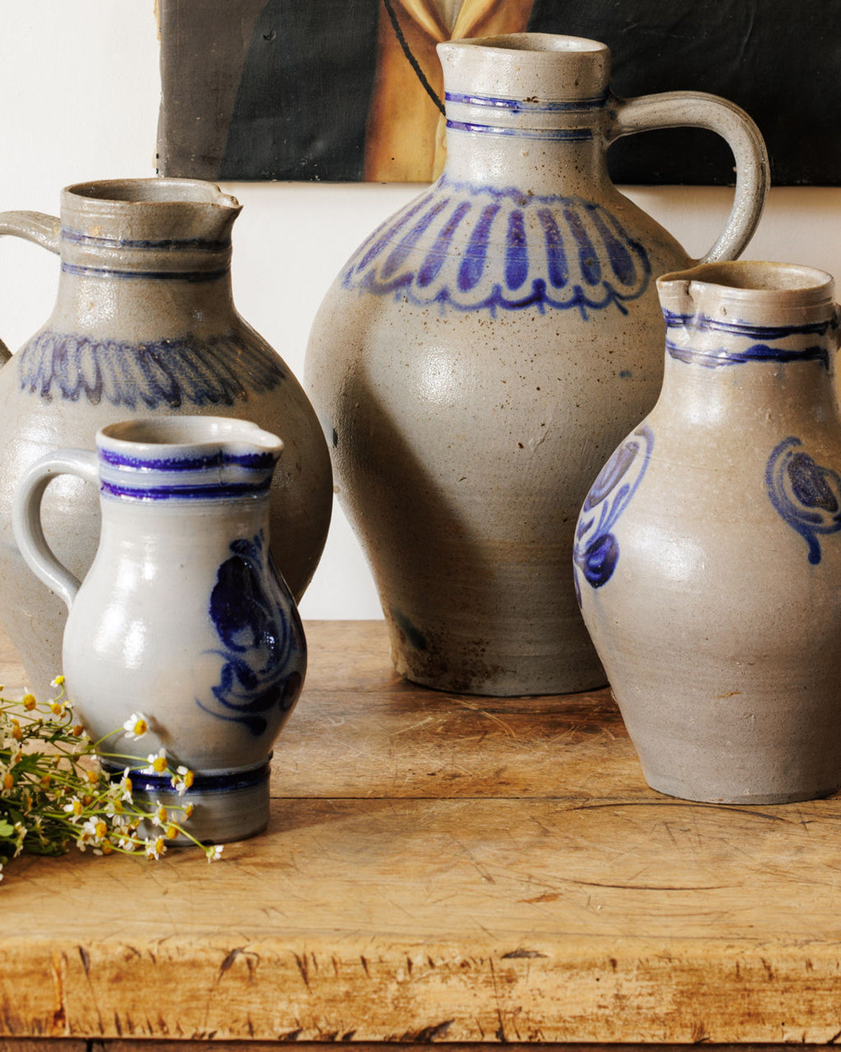 Four grey pottery jugs with blue patterns on a wooden table, next to chamomile flowers.