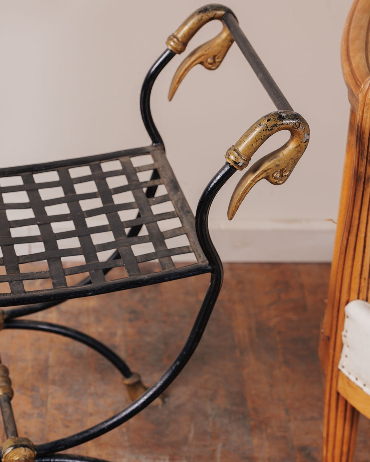 Black metal stool with a woven seat and gold bird-head armrests.