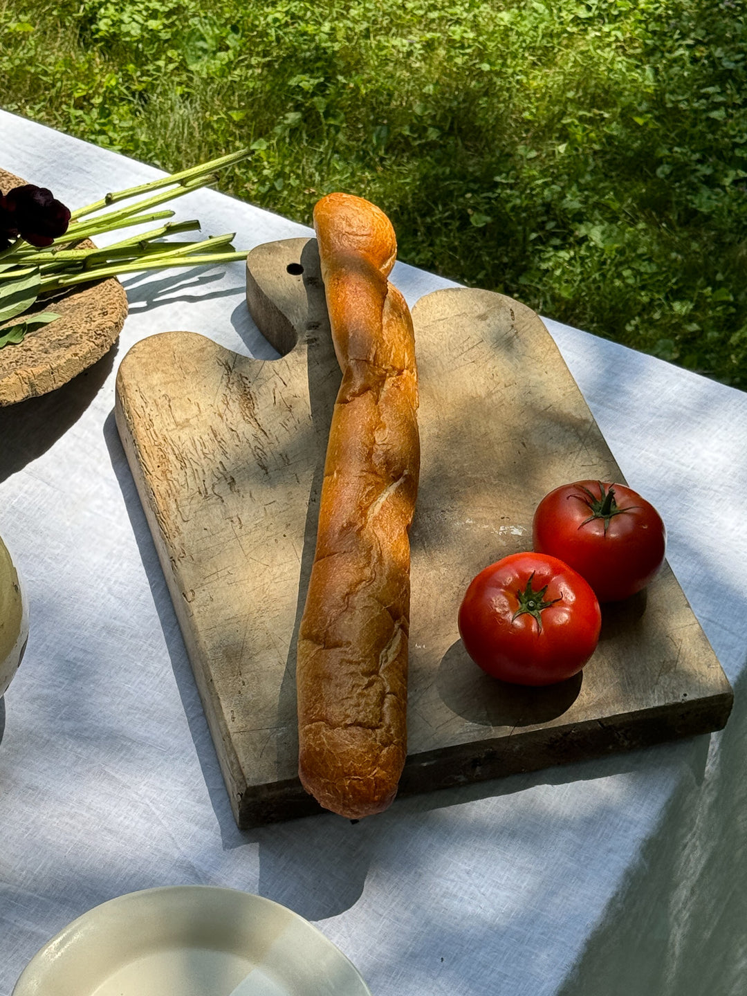 a loaf of bread and two tomatoes on a wooden cutting board on a table .