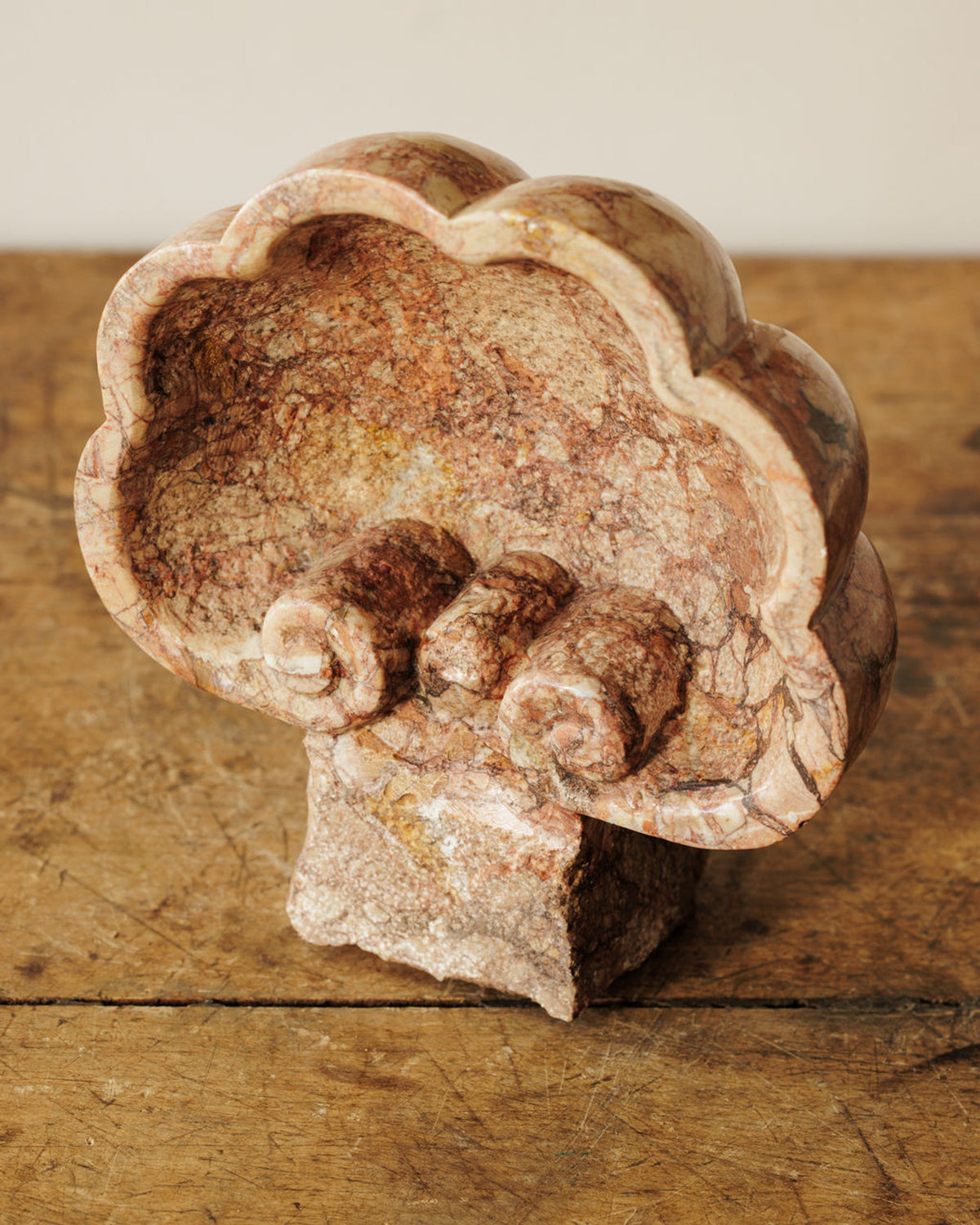 Reddish-brown veined marble sculpture of a wavy-rimmed bowl with three interior cylindrical forms, on wood.