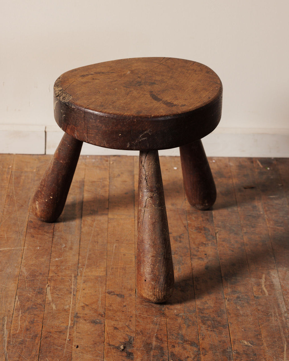 A rustic three-legged wooden stool with a thick, round seat.