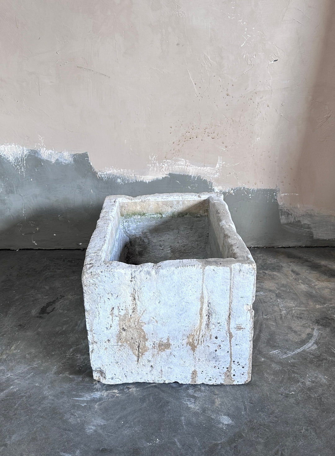 a white stone planter is sitting on a concrete floor in front of a wall .