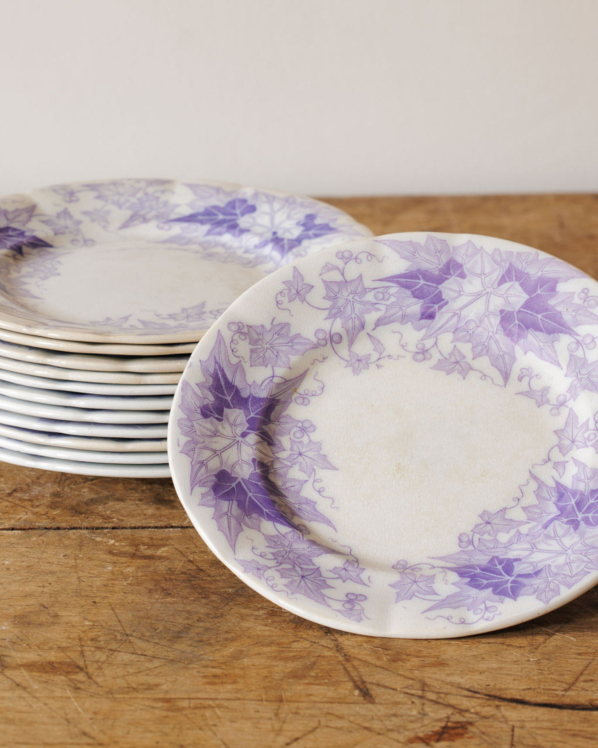White plates with purple ivy leaf patterns, stacked and one in the foreground, on a wooden table.