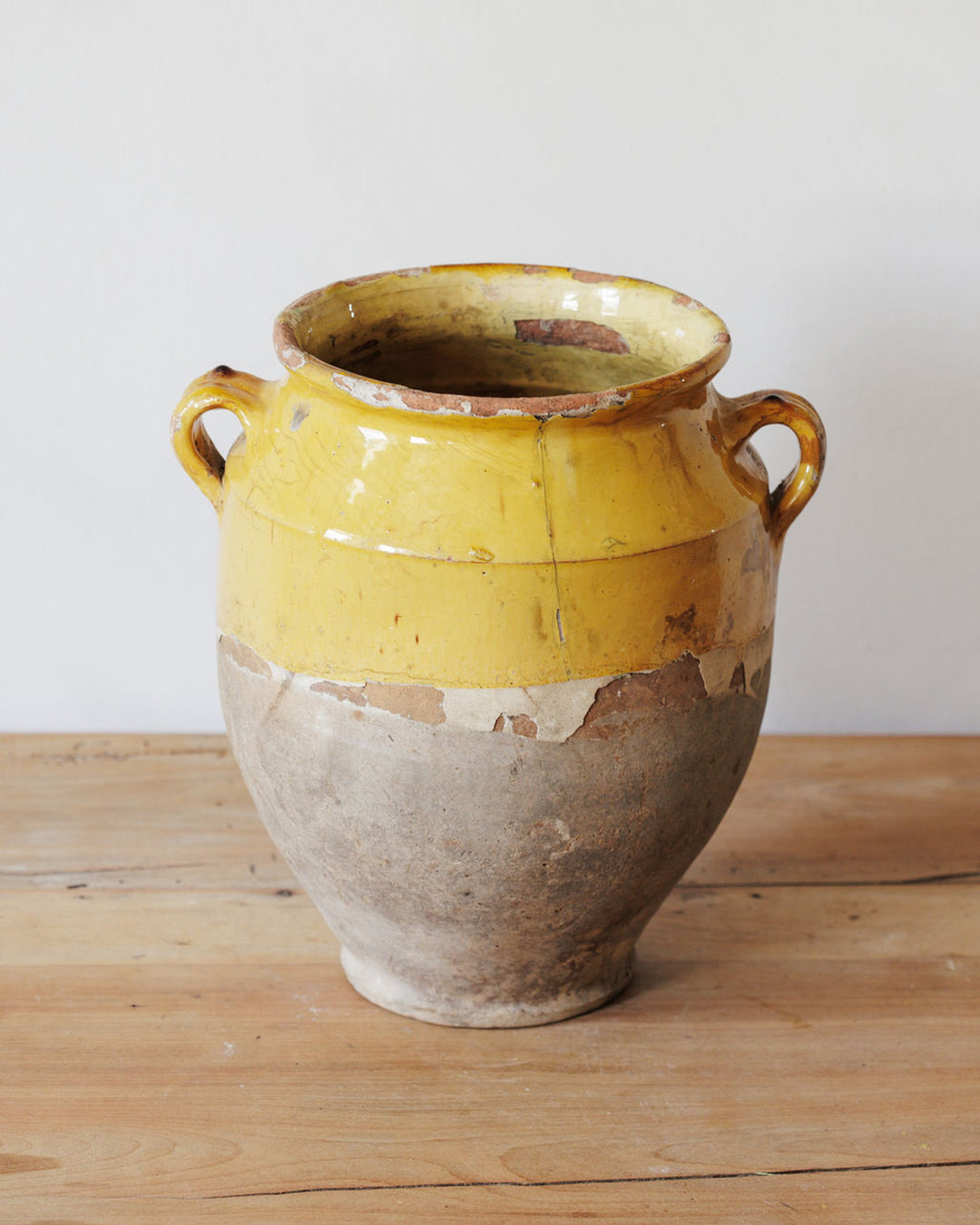 A distressed yellow and natural clay pot with two handles on a wooden surface.