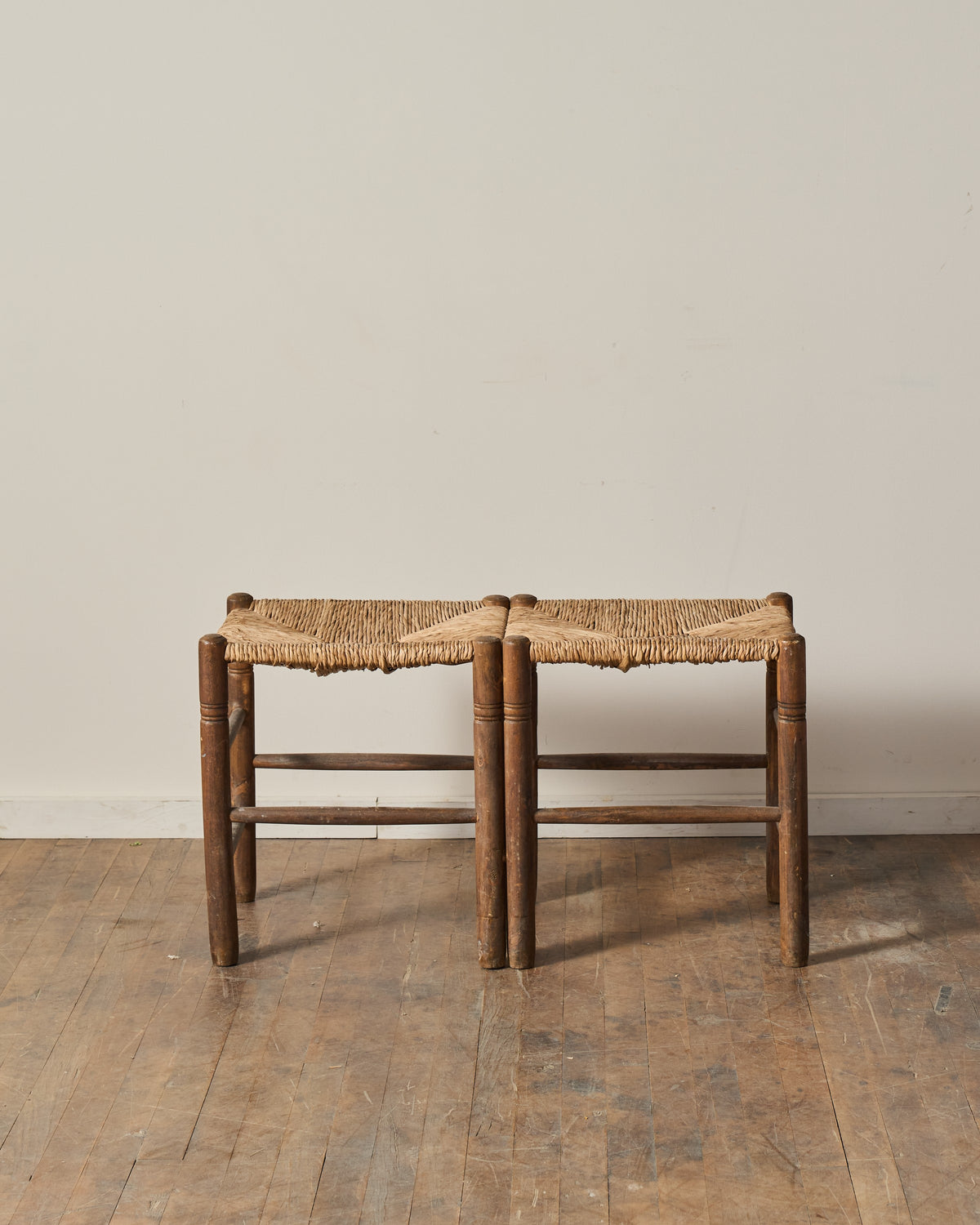 Two dark wooden stools with woven rush seats sit side by side on a wooden floor.