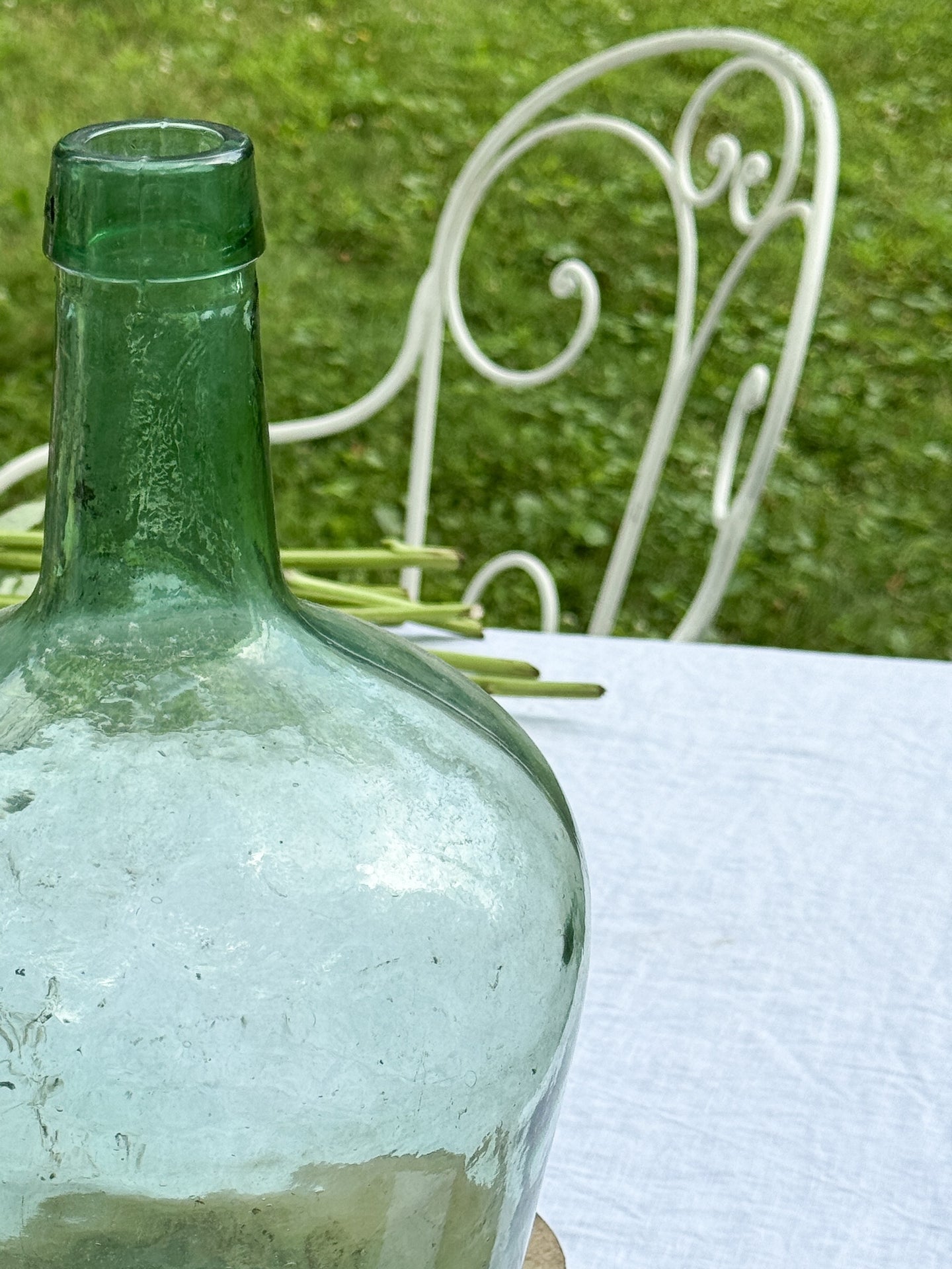 a green glass bottle is sitting on a table next to a white chair .