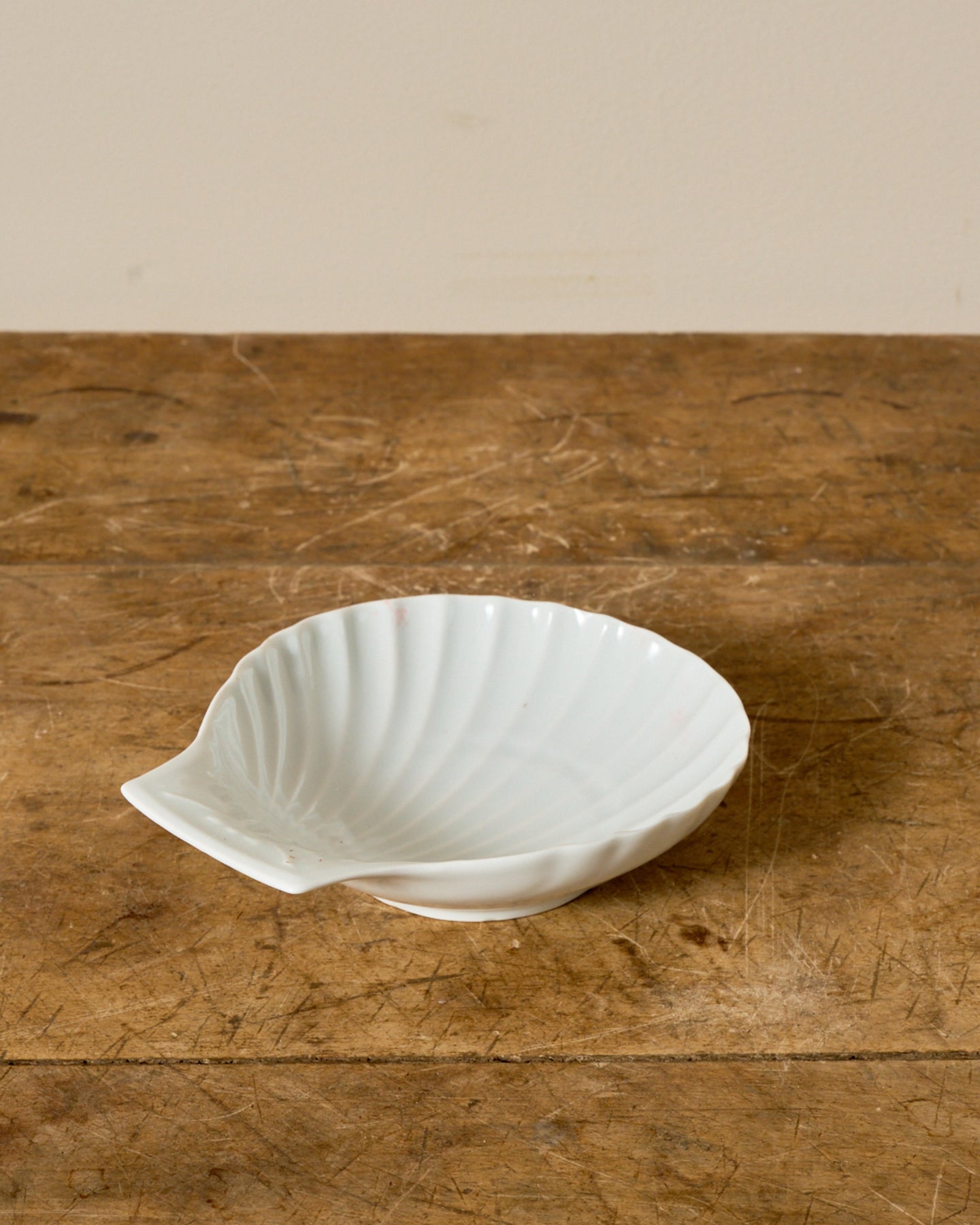 A white scallop shell dish on a wooden table.