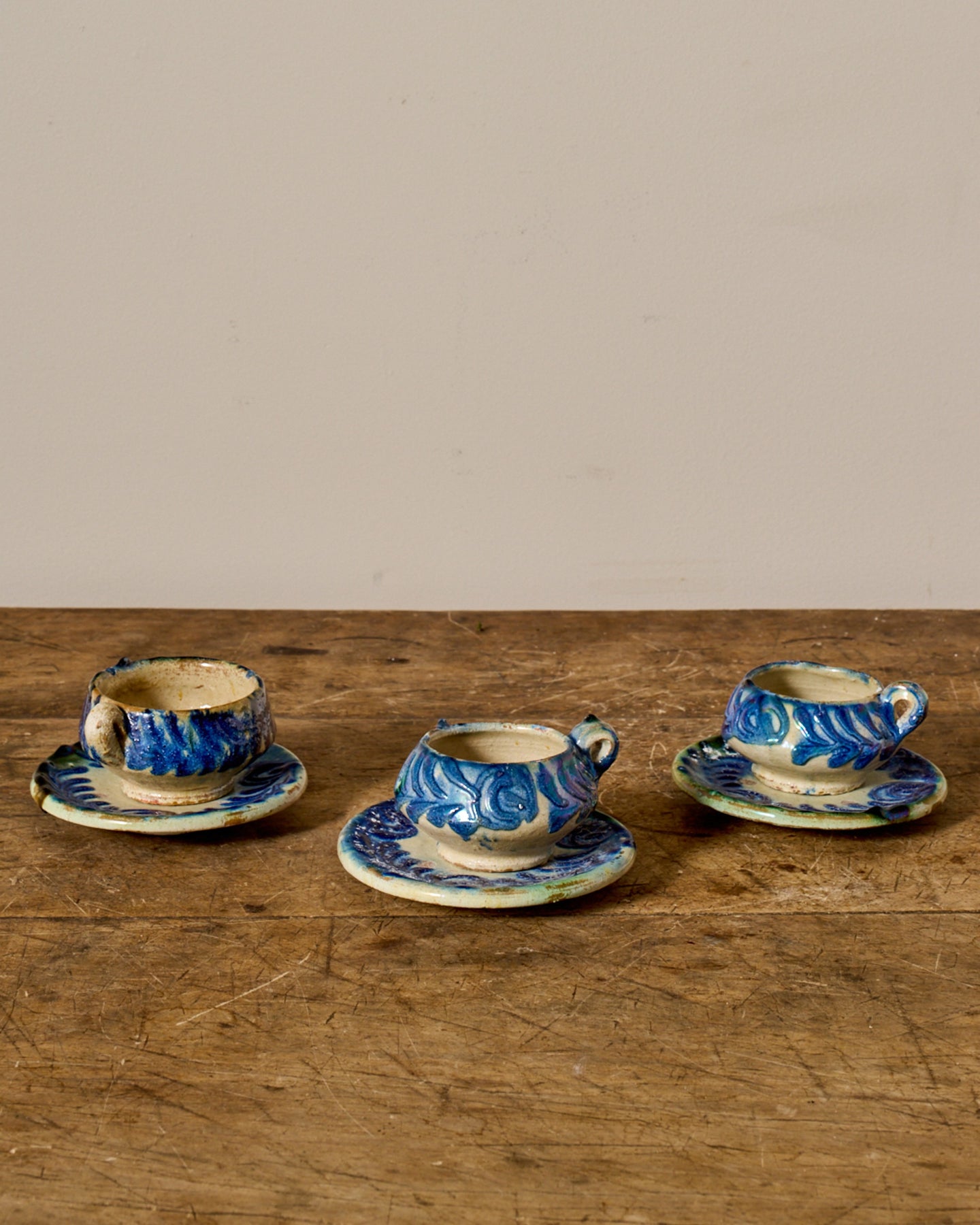 Three miniature blue and white patterned ceramic cups and saucers on a wooden table.