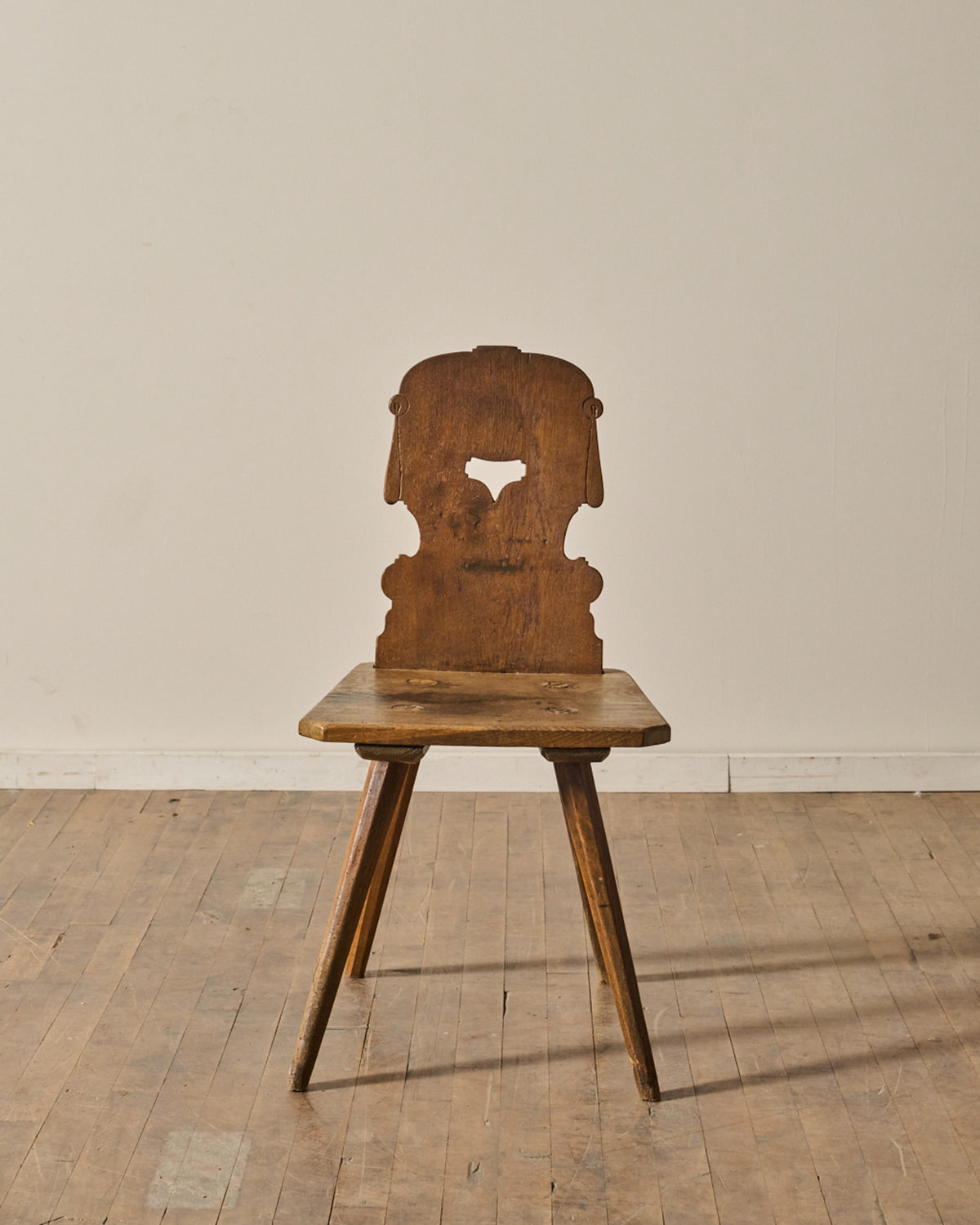 Rustic wooden chair with a carved backrest featuring a heart cutout and three splayed legs.