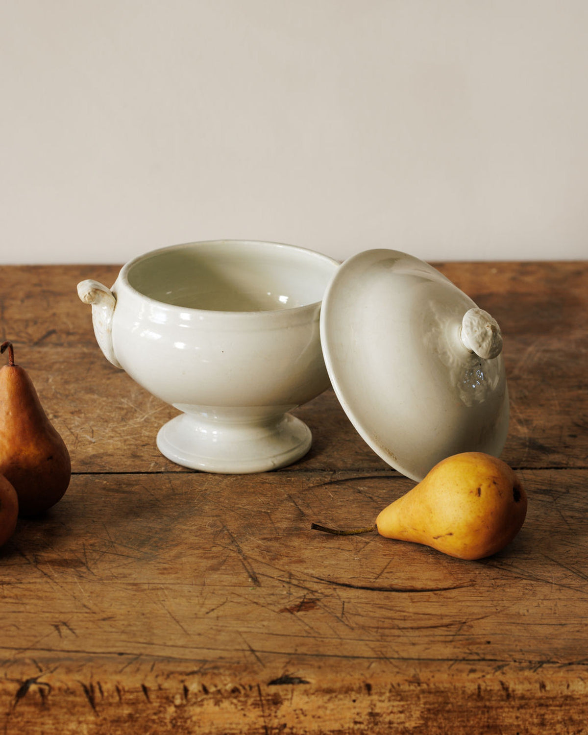 A white ceramic lidded bowl with pears on a distressed wooden table.