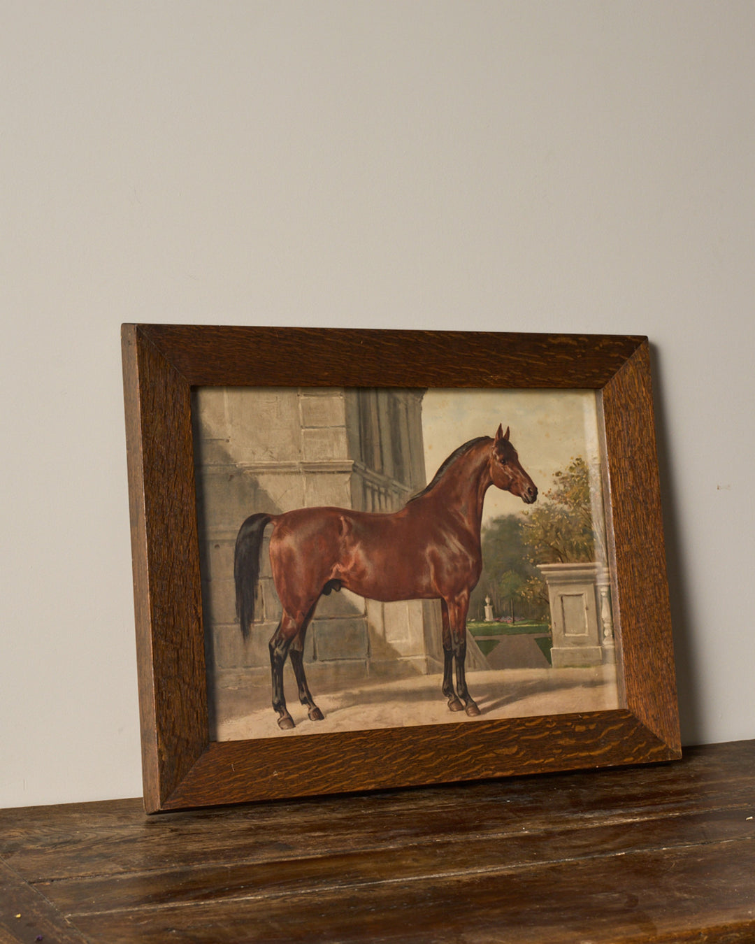 Dark wood framed painting of a brown horse in a classical garden setting.