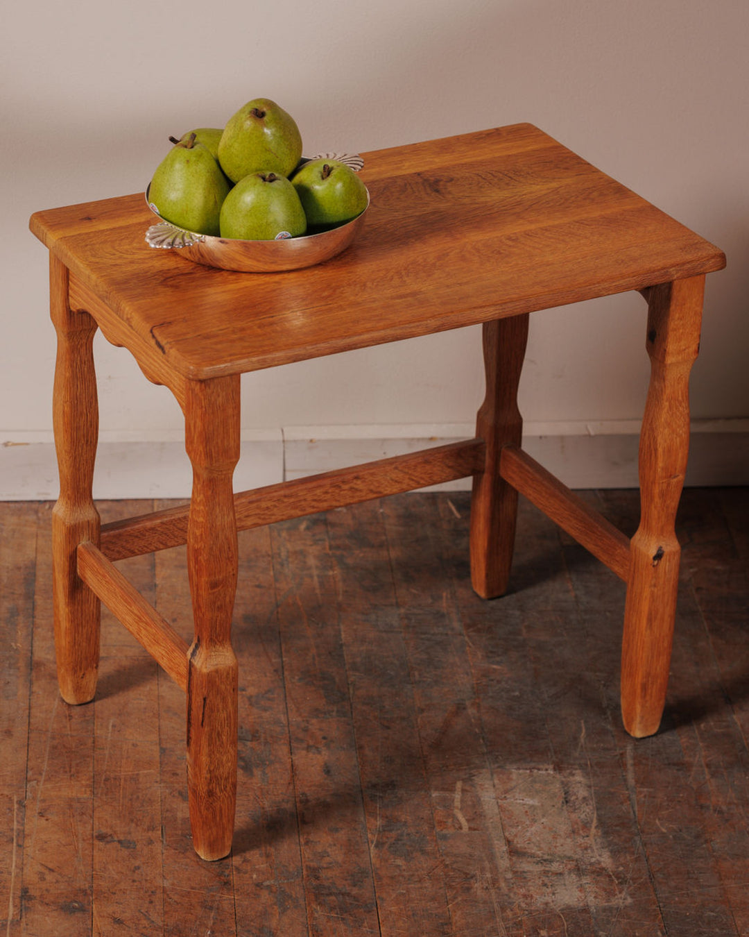 A light brown wooden table with a silver bowl of green pears.