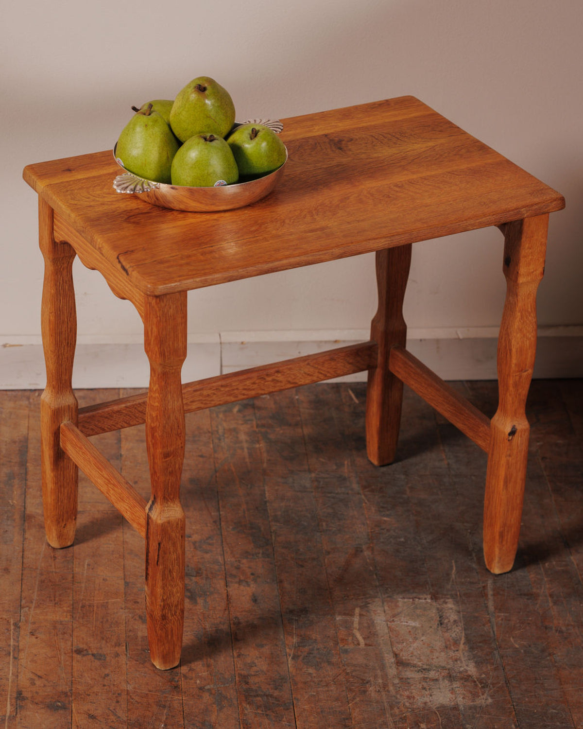 A light brown wooden table with a silver bowl of green pears.