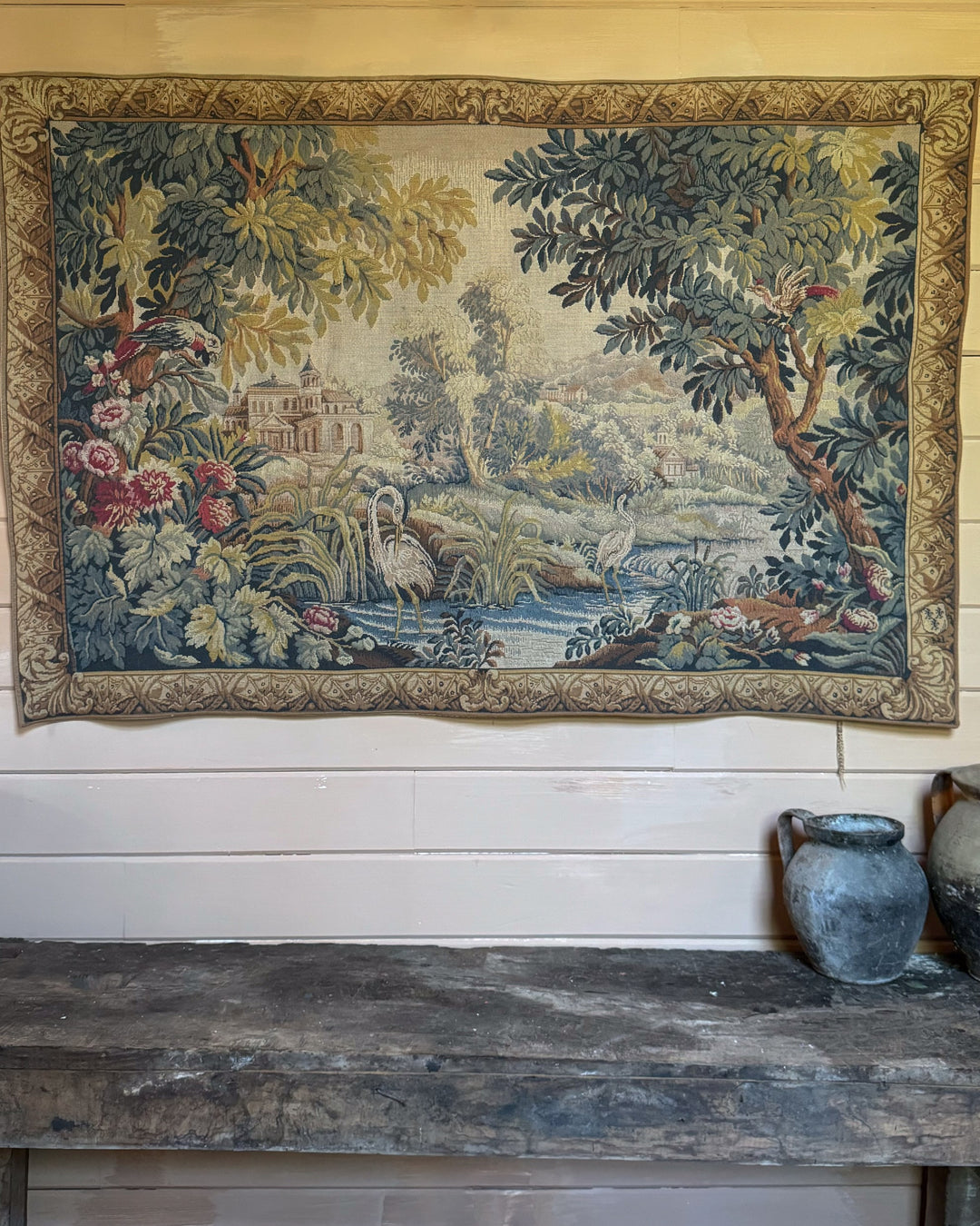 a french tapestry is hanging on a wall above a wooden table .