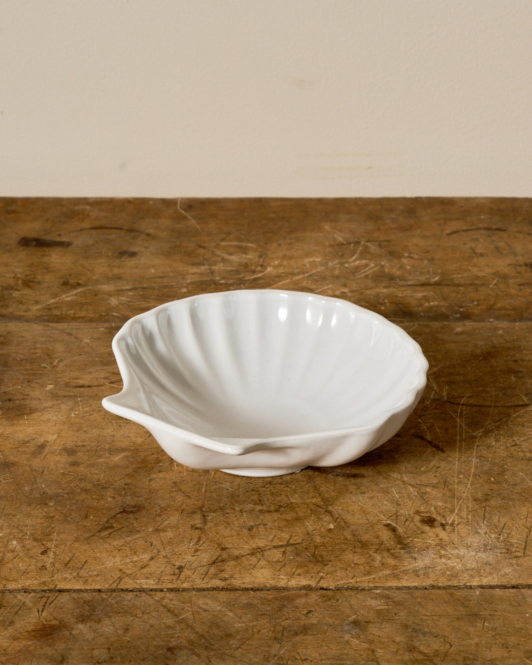 A white, shell-shaped bowl on a rustic wooden table.