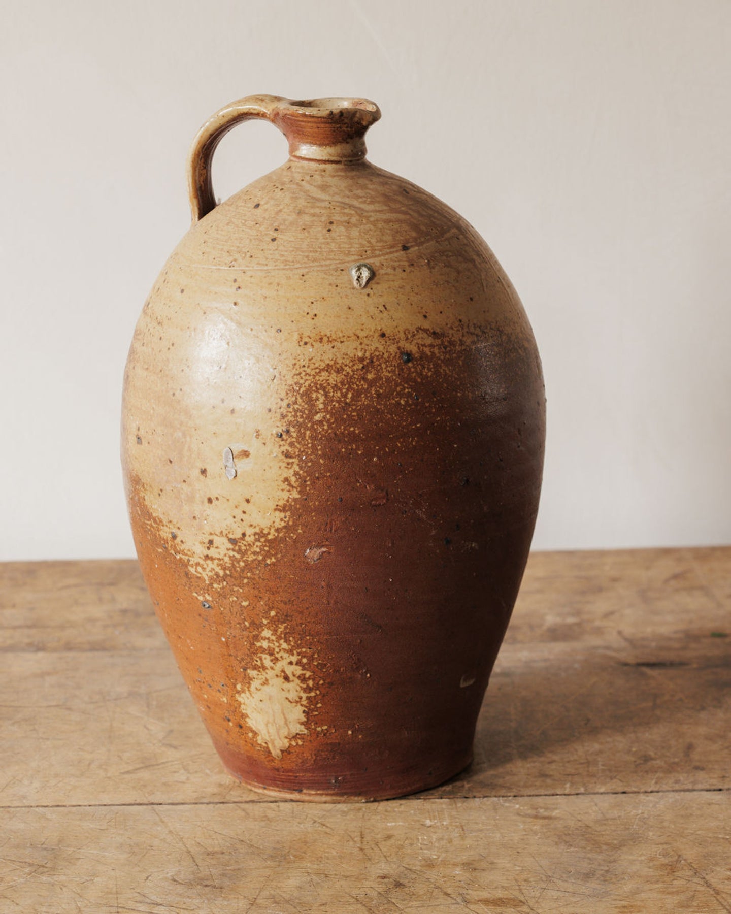 Rustic two-tone brown stoneware jug on a wooden surface.