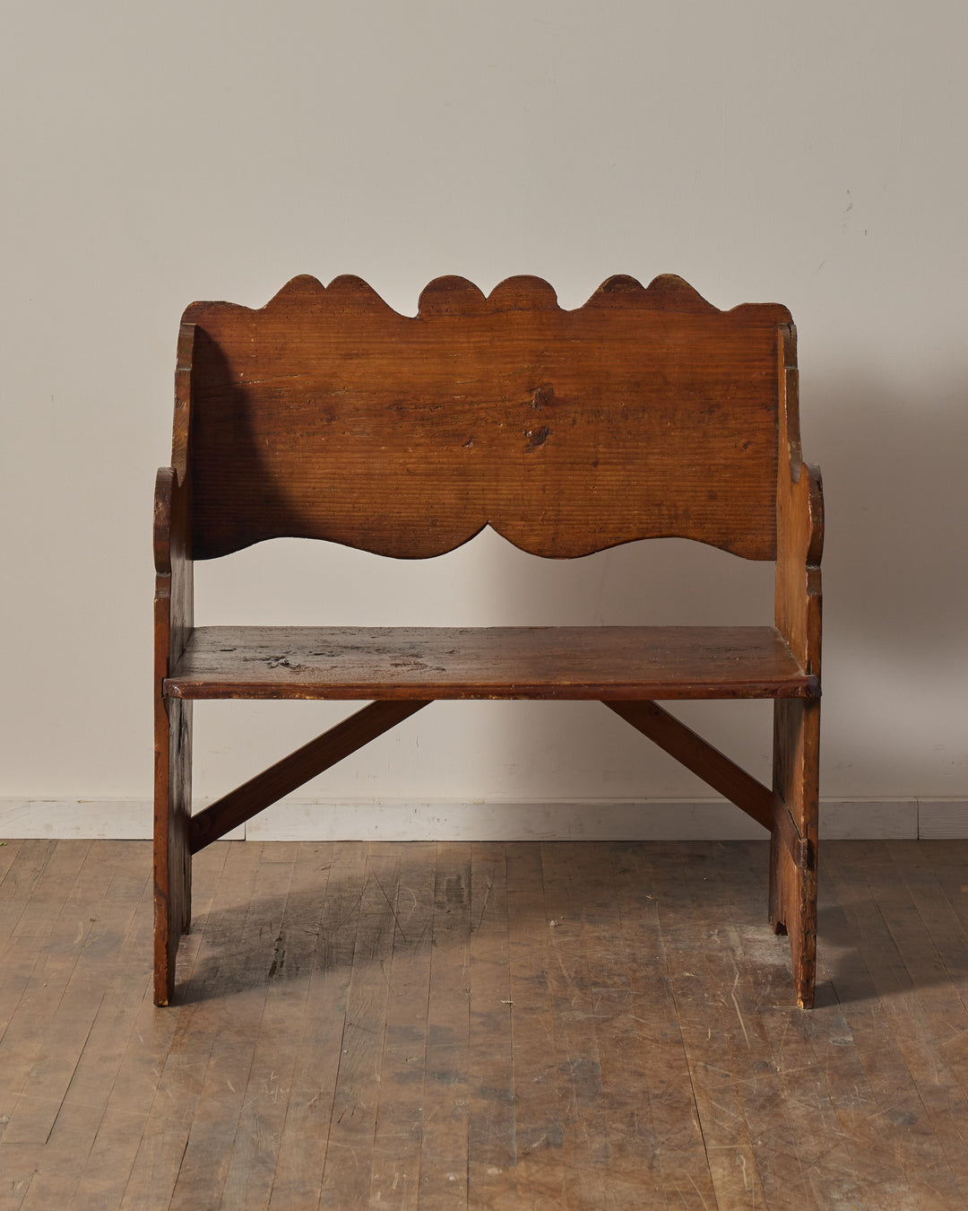A rustic dark wood bench with a scalloped backrest.