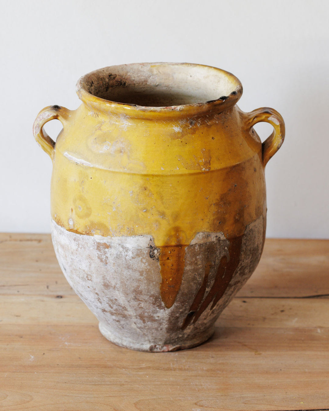 Rustic yellow and natural clay two-handled pot on a wooden surface.