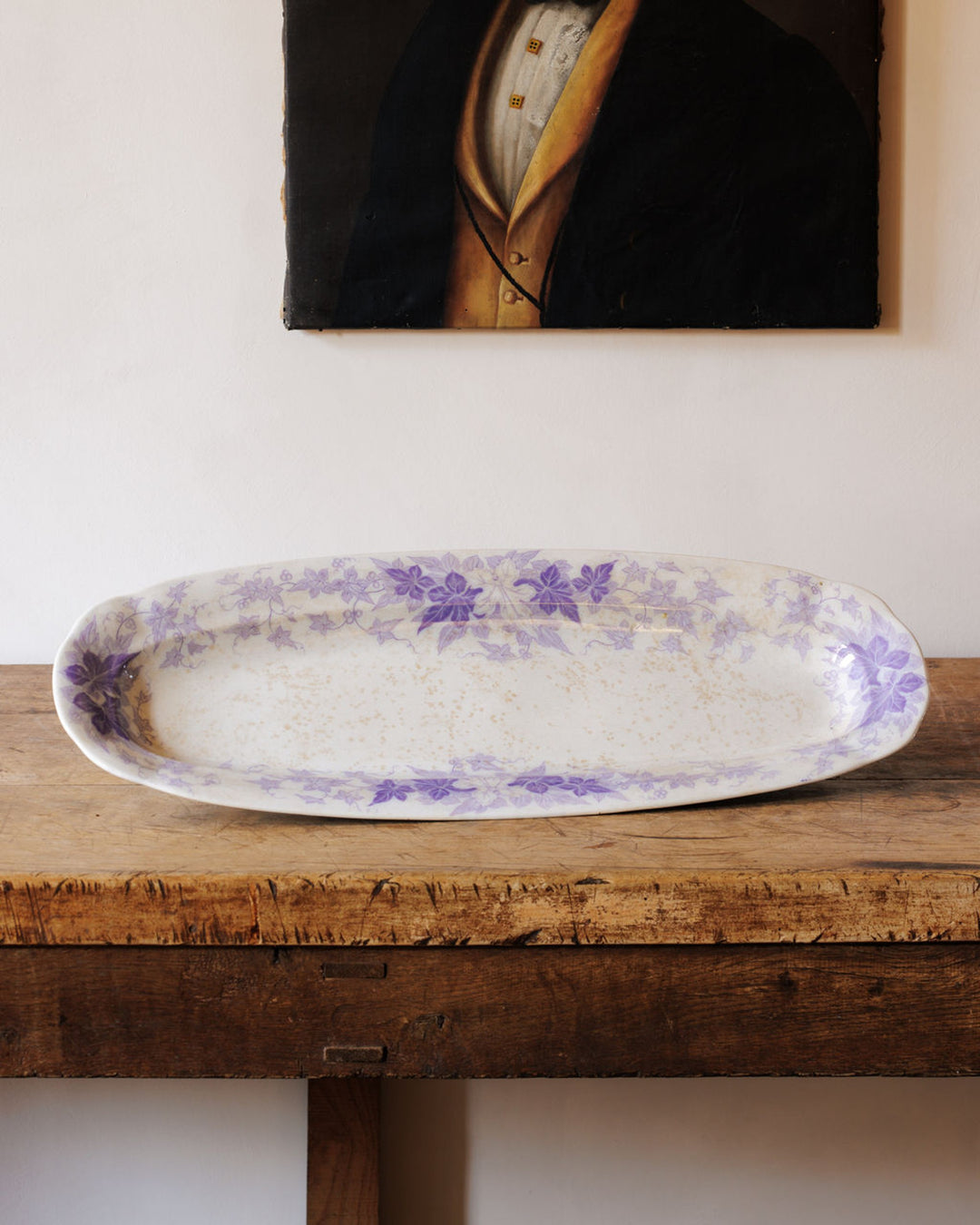 White oval serving platter with purple floral designs and speckled details on a rustic wooden table.