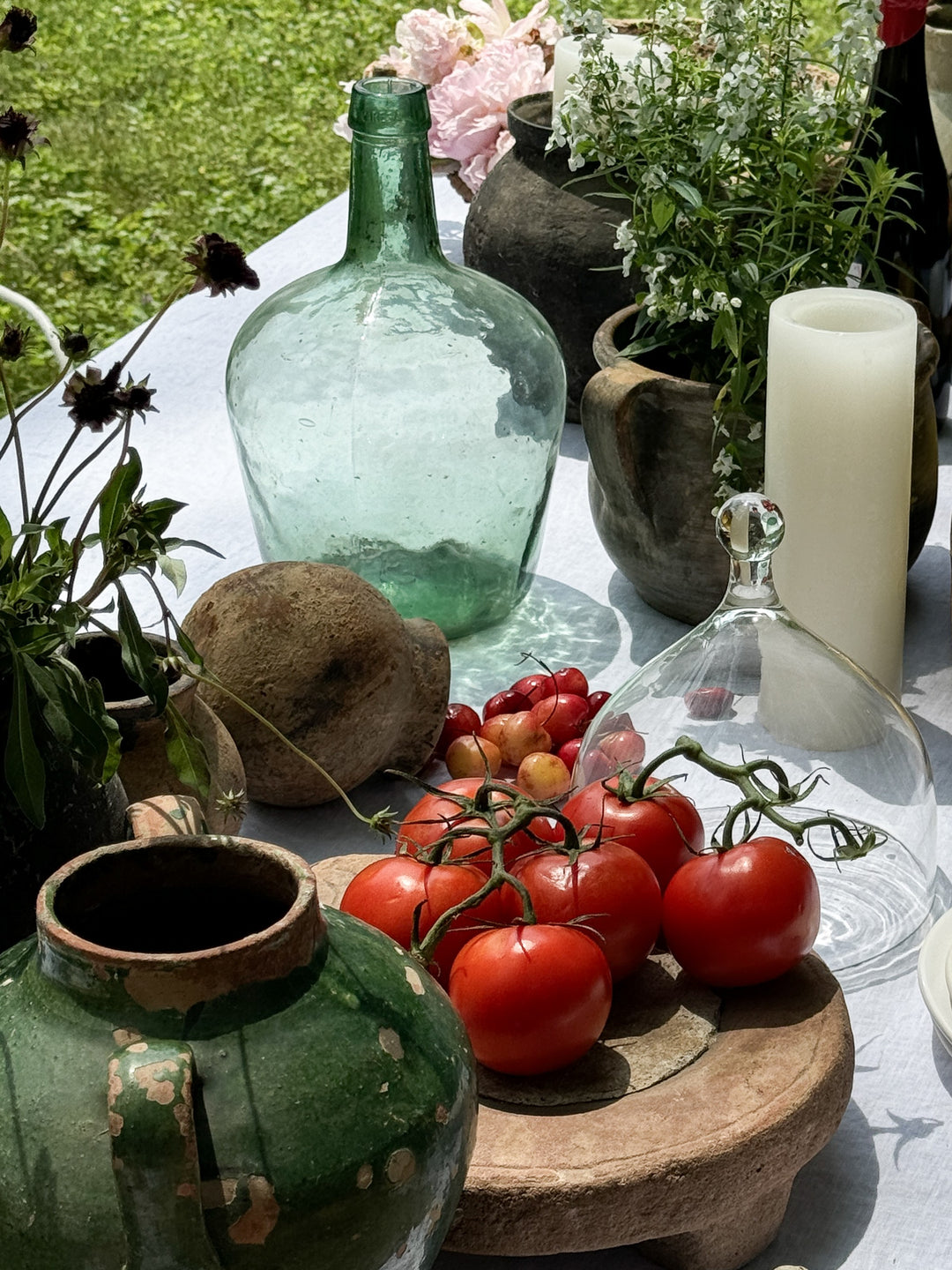 a table with tomatoes , vases , candles and flowers on it