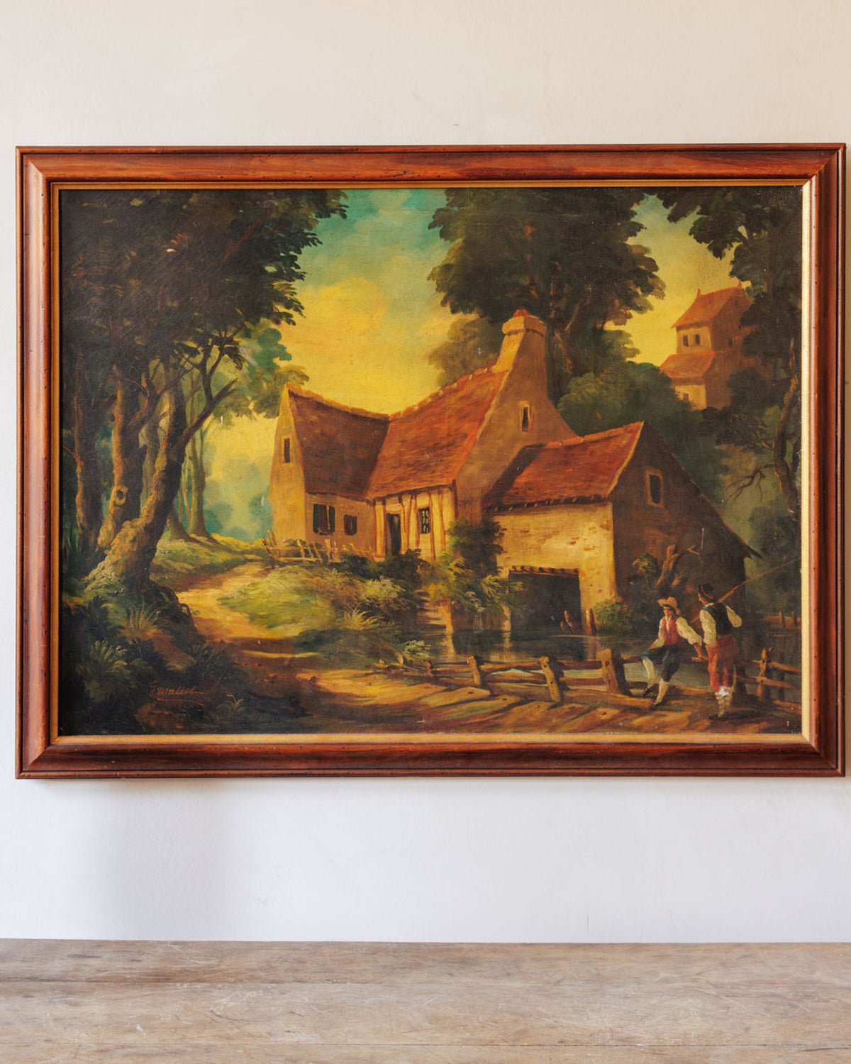 Framed painting of a rustic house with a red roof, surrounded by trees, with two figures by a stream and a winding path.