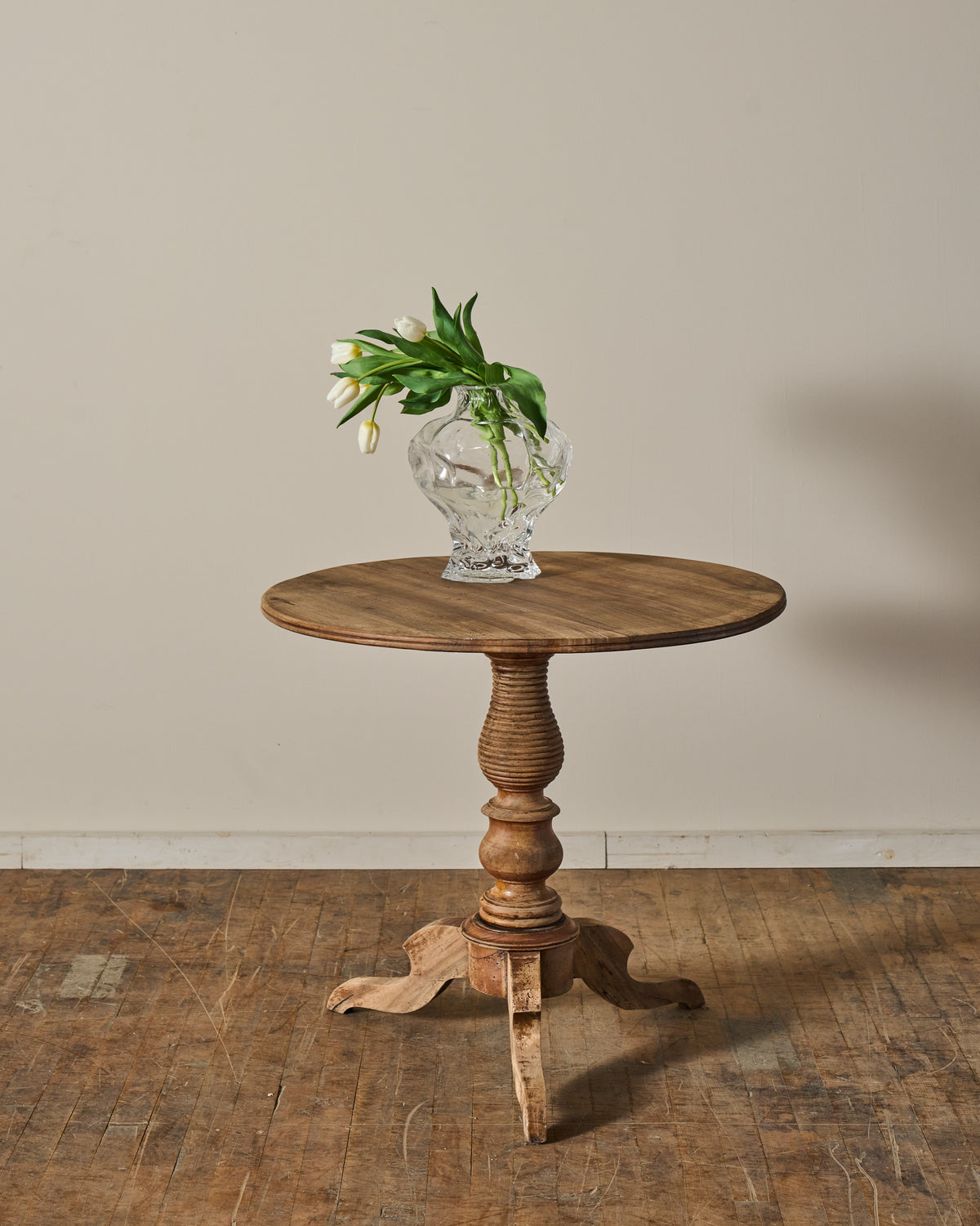 A round wooden pedestal table with a clear vase of white tulips.