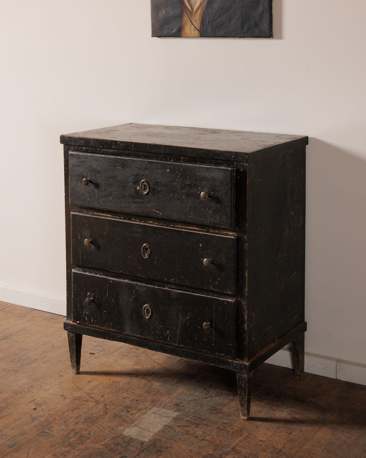 A distressed black wooden dresser with three drawers and metal pulls on a wooden floor.