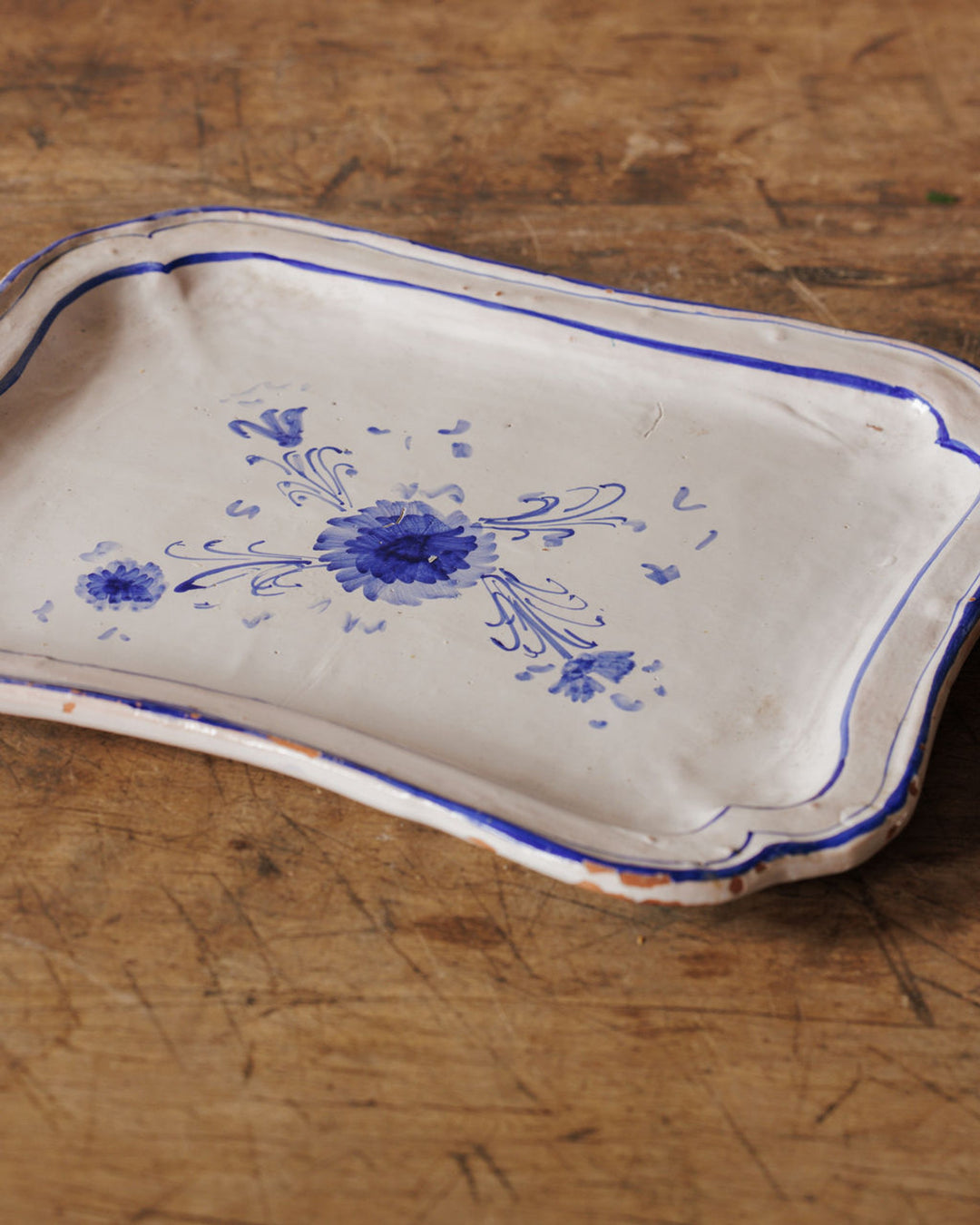 White ceramic tray with wavy edges and blue floral designs on a wooden surface.