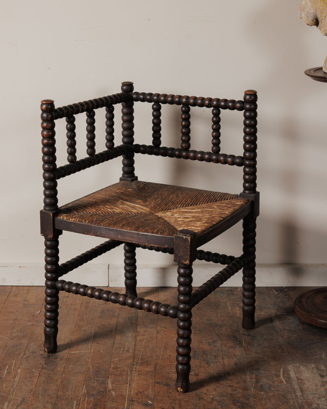 Dark wood bobbin corner chair with a woven straw seat.