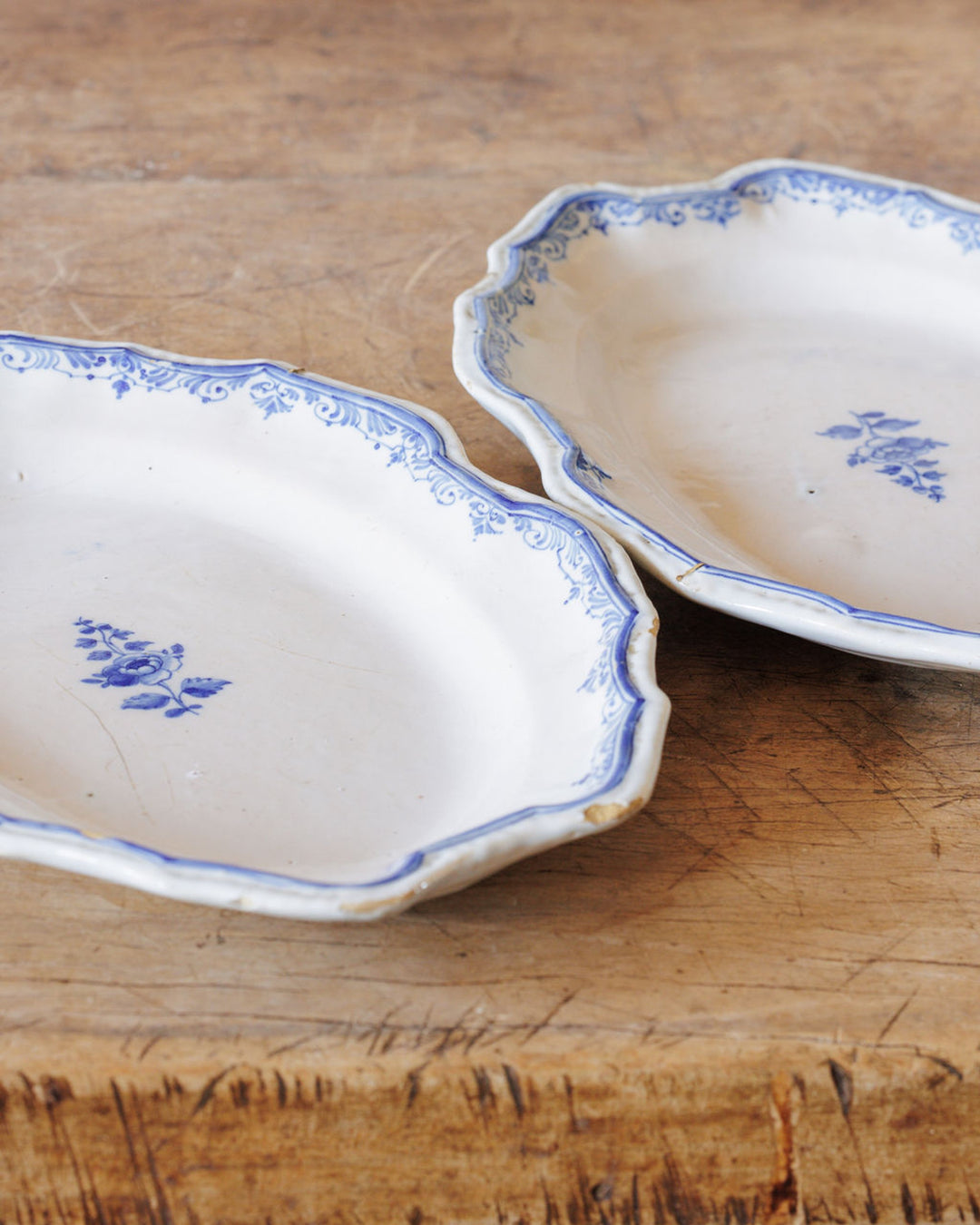 Two vintage white oval dishes with blue floral patterns and scalloped edges, on a wooden surface.